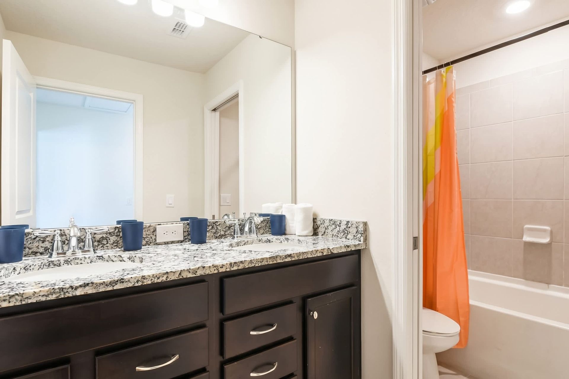 Modern bathroom with dual sinks, granite counters, and a tub-shower combo.