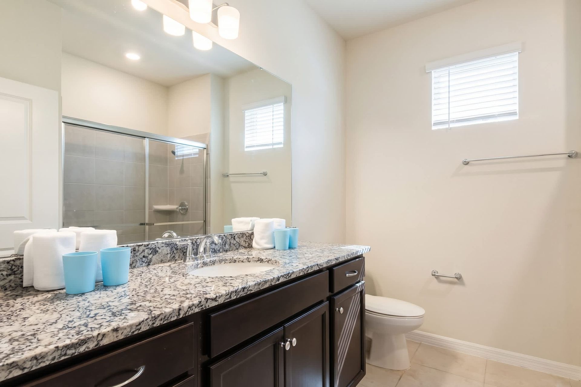 Bright bathroom with granite counters, double sinks, and a walk-in glass shower.