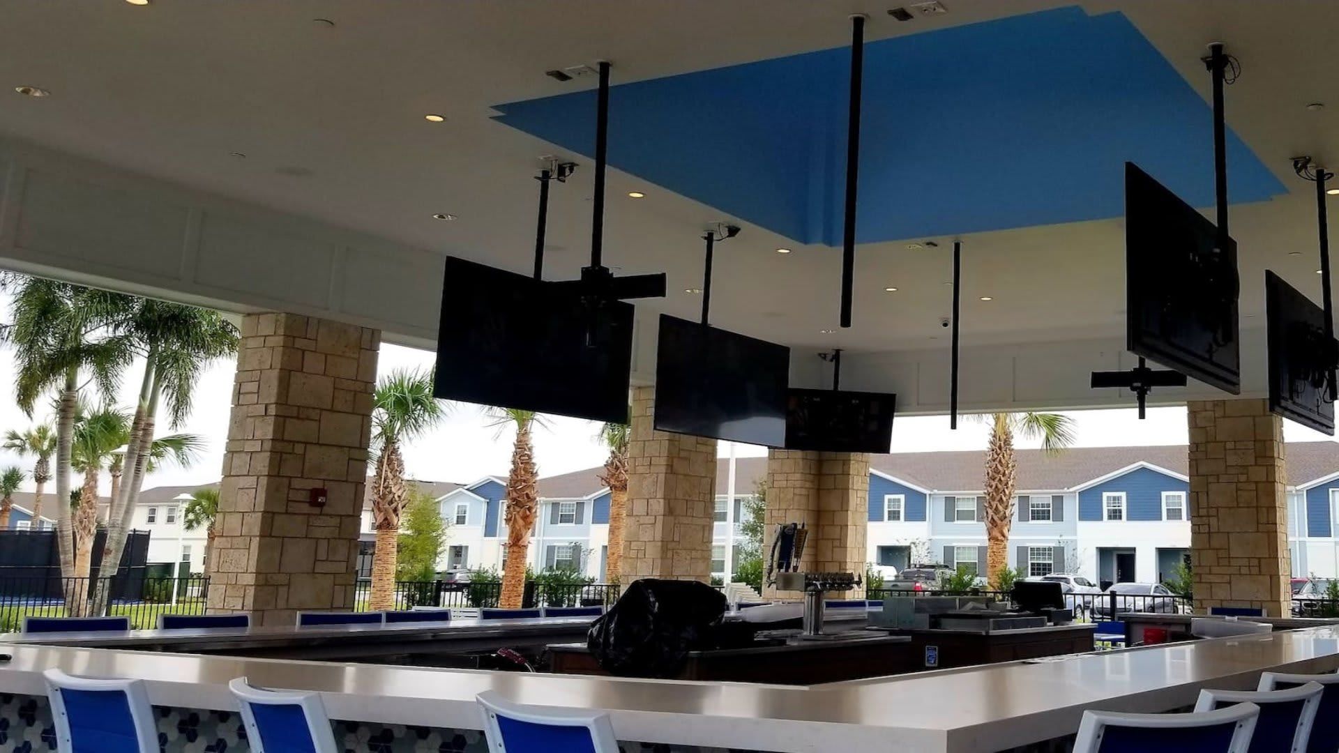 Open-air resort bar with multiple TVs, modern seating, and views of palm trees

