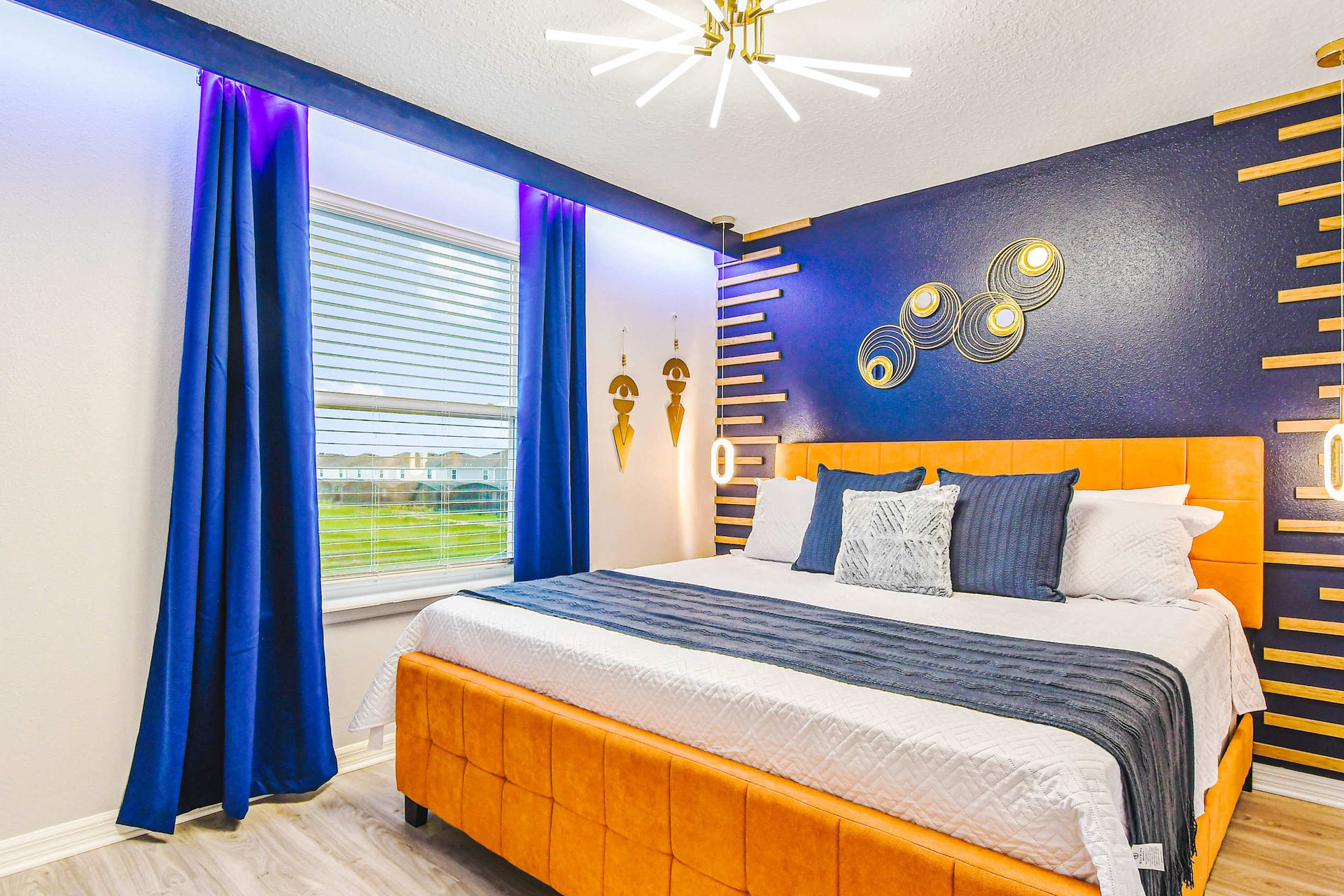 Bold and modern bedroom with a navy and gold accent wall, mustard upholstered bed, and contemporary lighting.