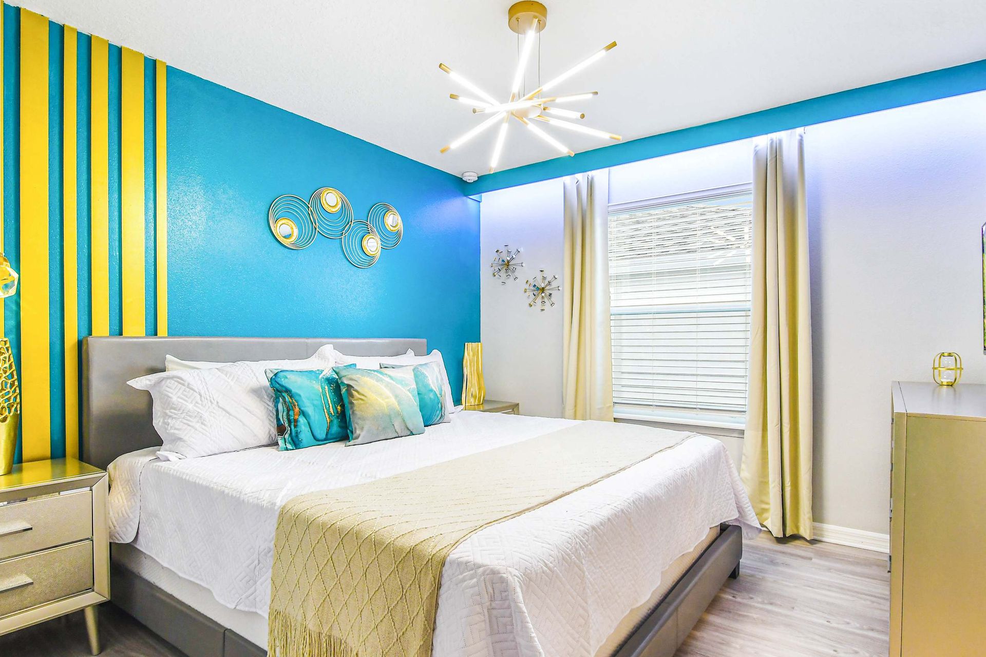 Vibrant modern bedroom with bold teal and gold accents, king bed, and luxe lighting.