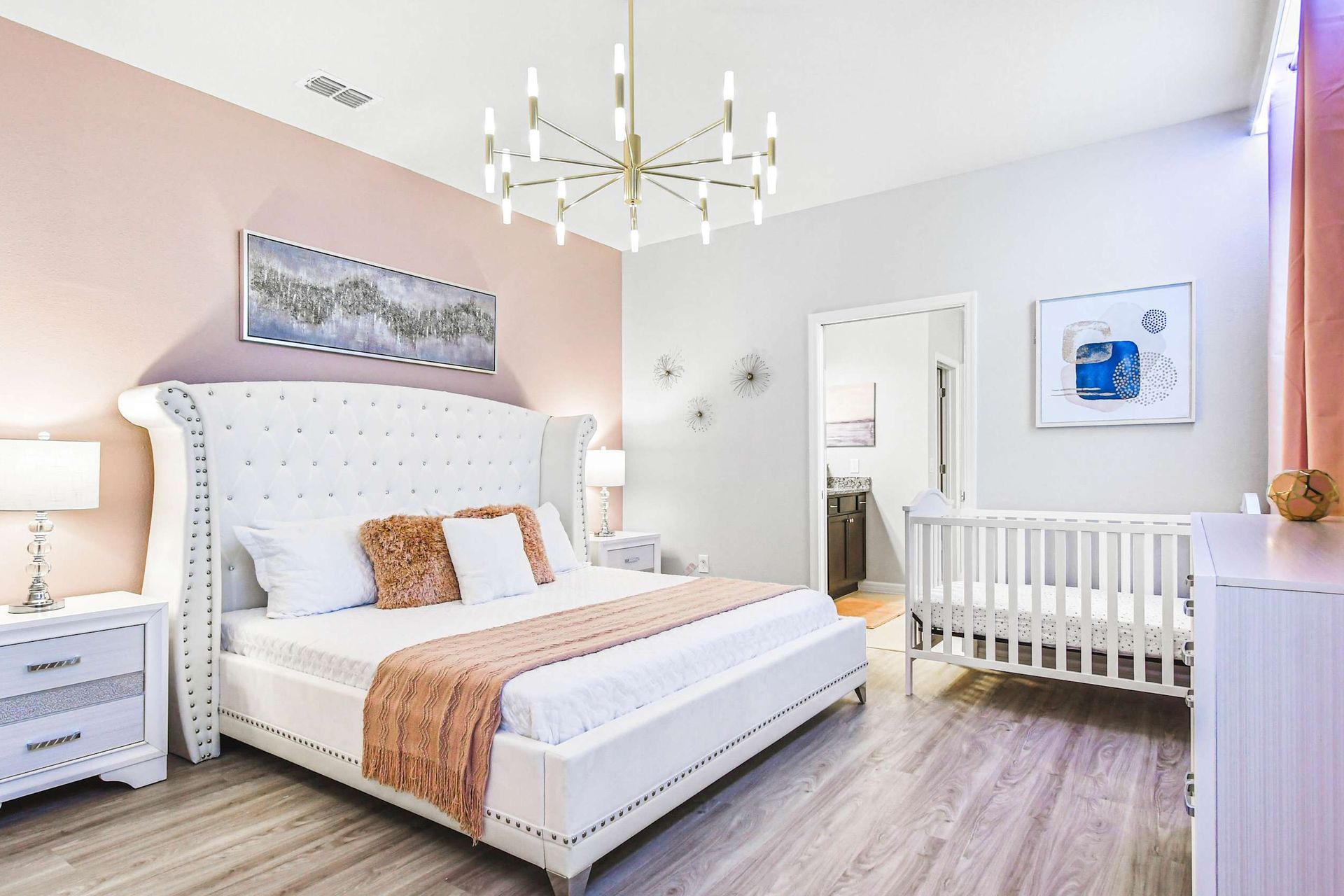 Elegant primary suite with plush king bed, modern decor, and cozy crib for baby.
