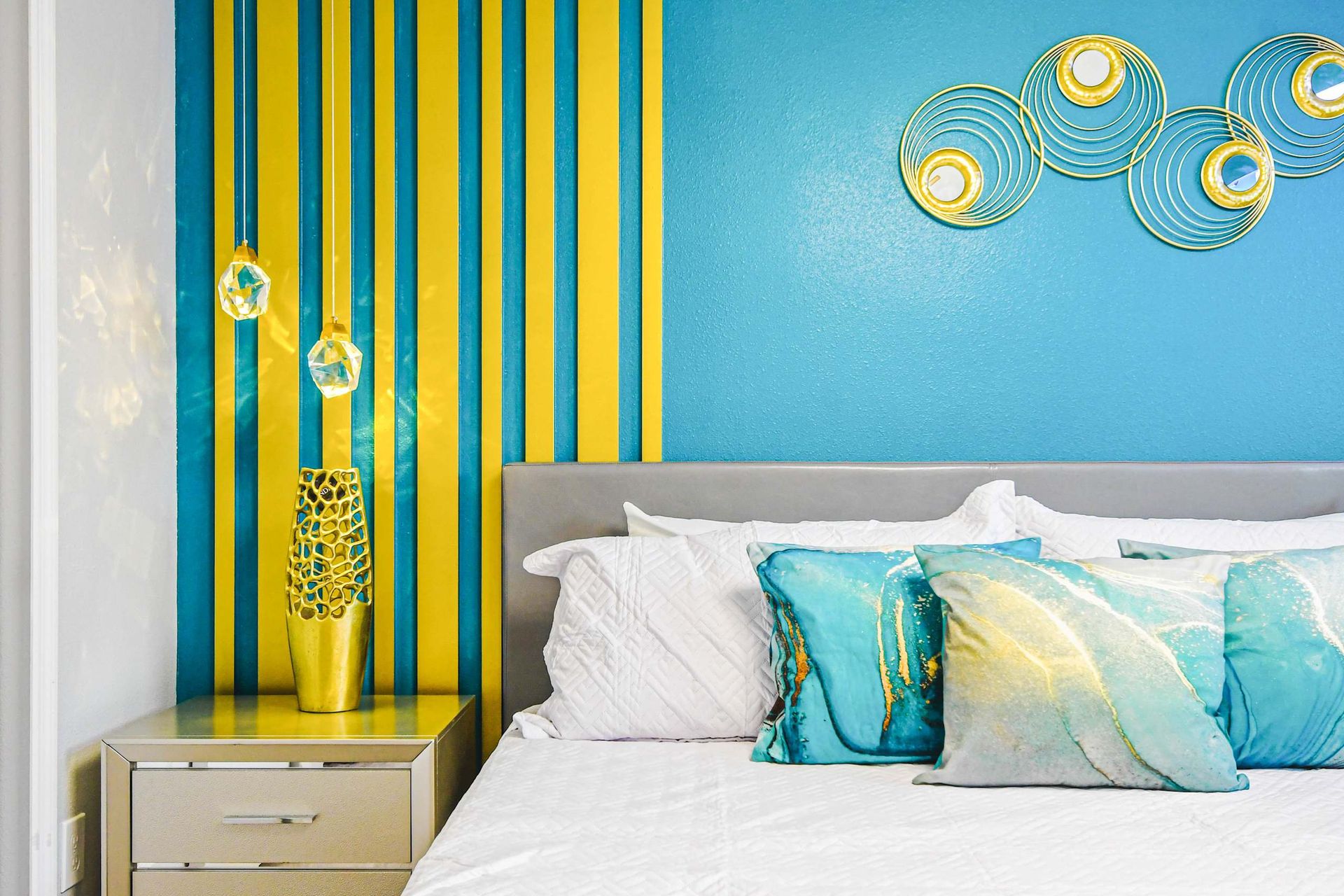 Chic bedroom with teal and gold accent wall, artistic pillows, and modern decor.