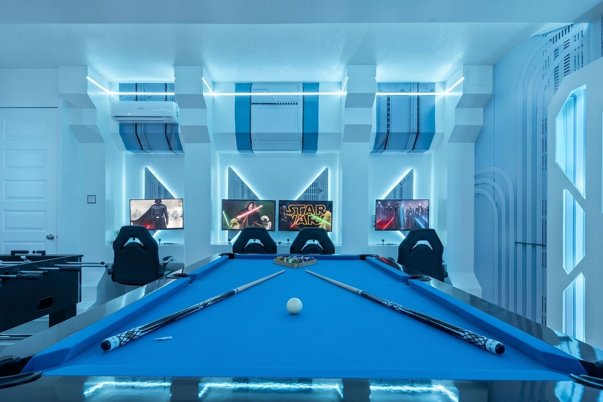 Blue-lit modern game lounge with pool and multiple screens.