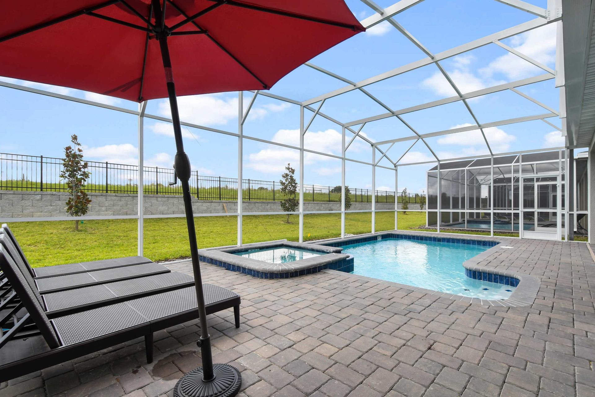 Sunny screened-in pool and spa with loungers and umbrella for ultimate relaxation.
