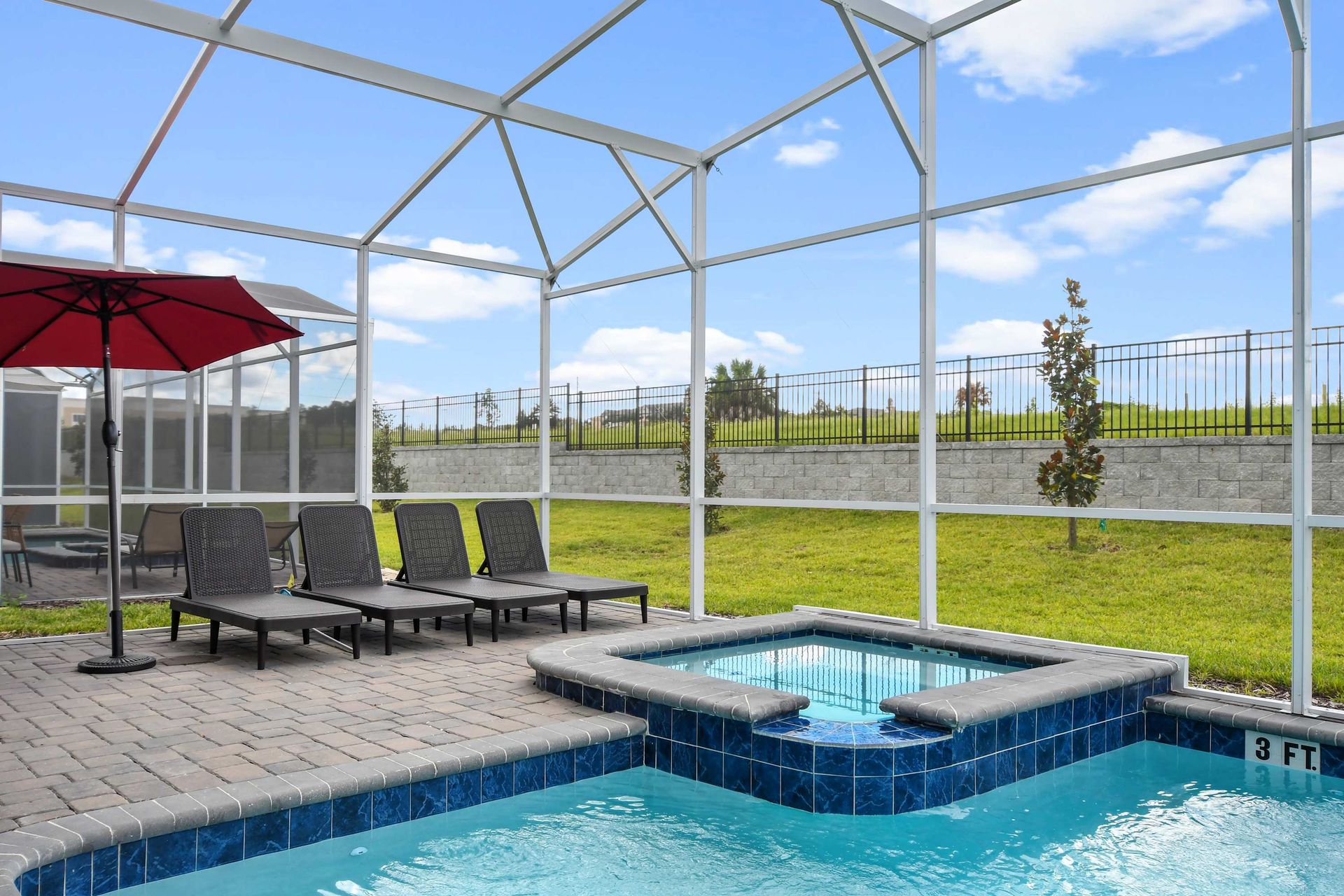 Relaxing screened-in spa and pool area with loungers, umbrella, and sunny views.
