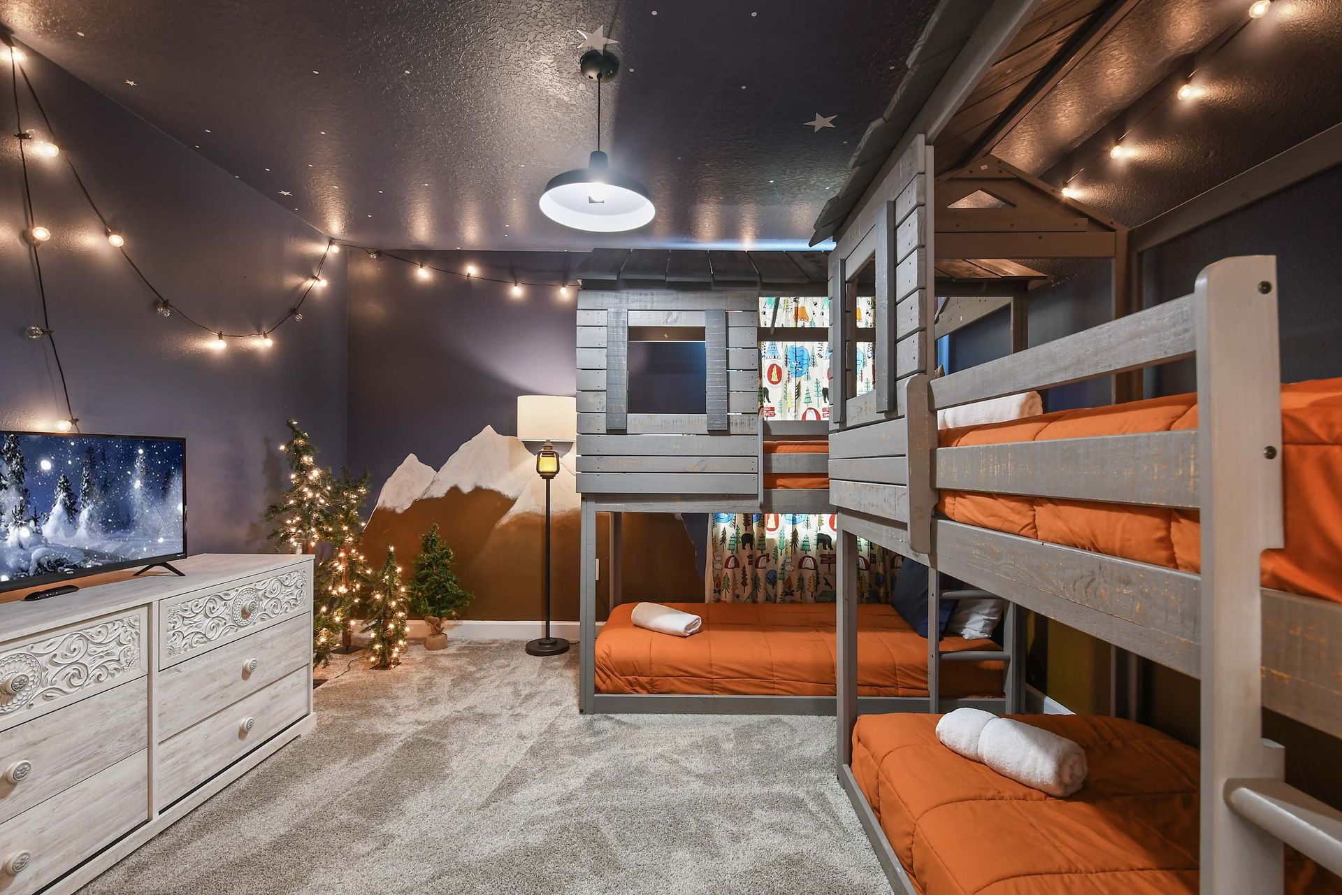 Cozy cabin-themed bunk room with twinkle lights, mountain mural, and playful vibes.
