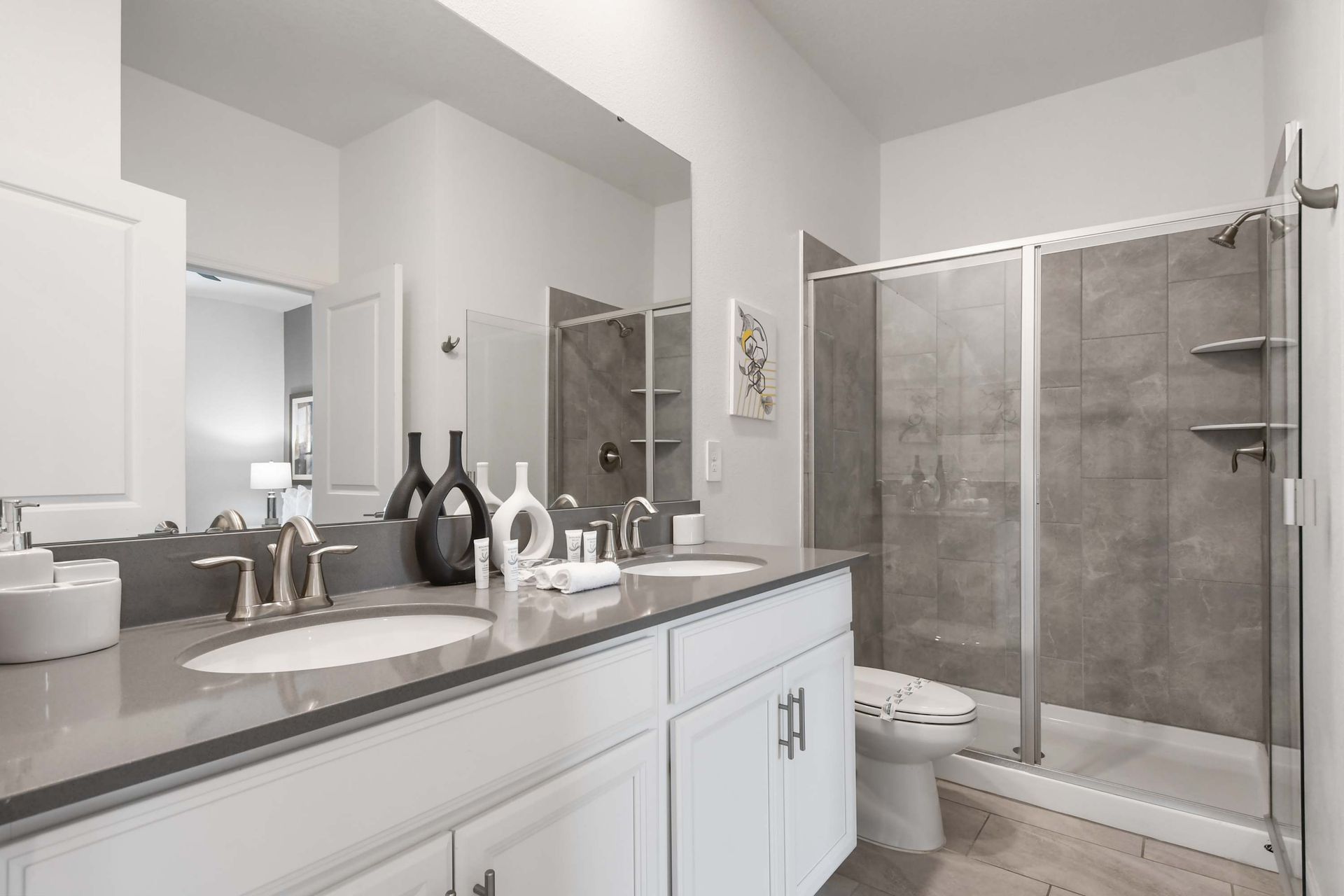 Modern bathroom with dual sinks, sleek gray countertops, and a spacious walk-in shower.
