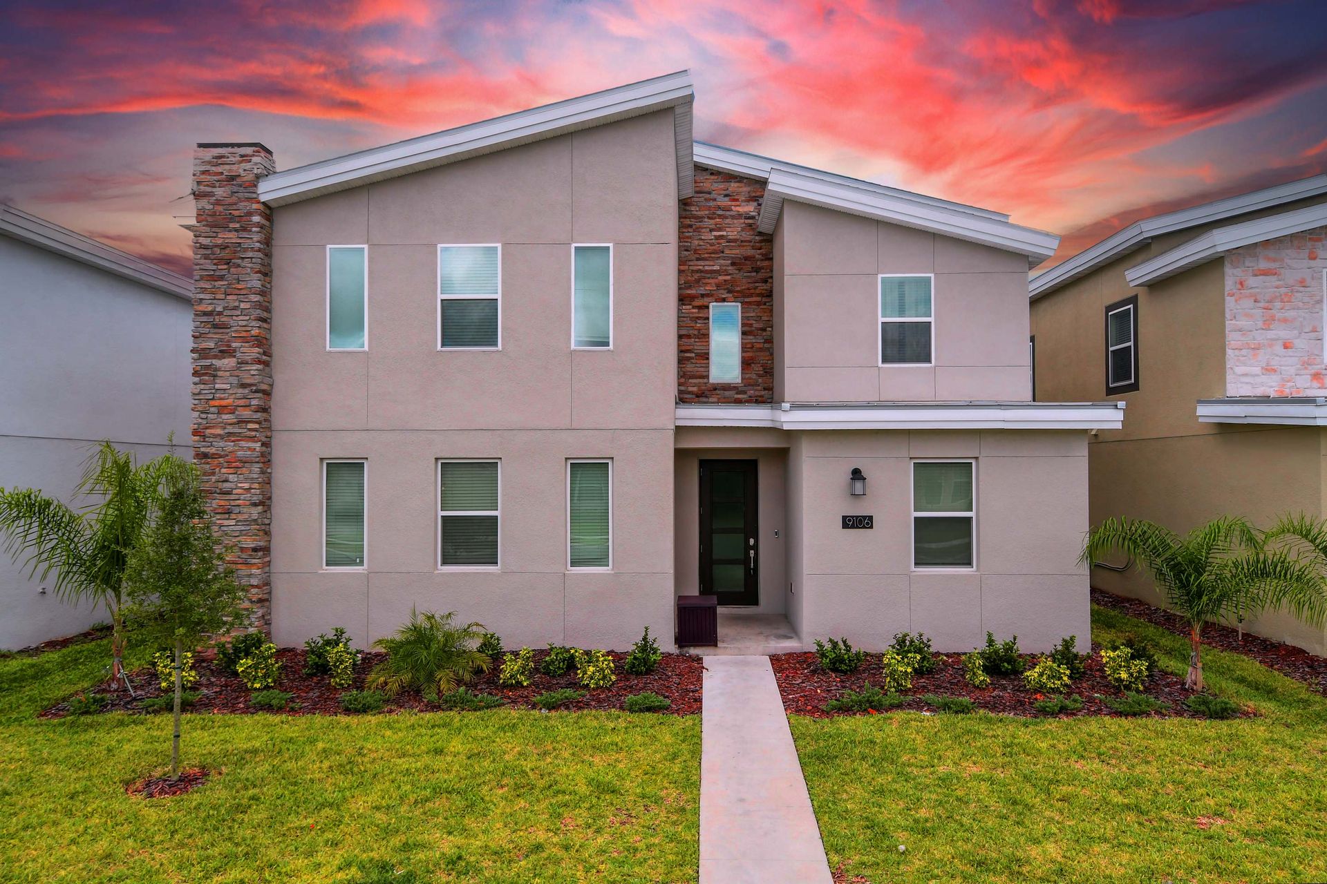Modern two-story retreat with stylish stone accents and stunning sunset backdrop.
