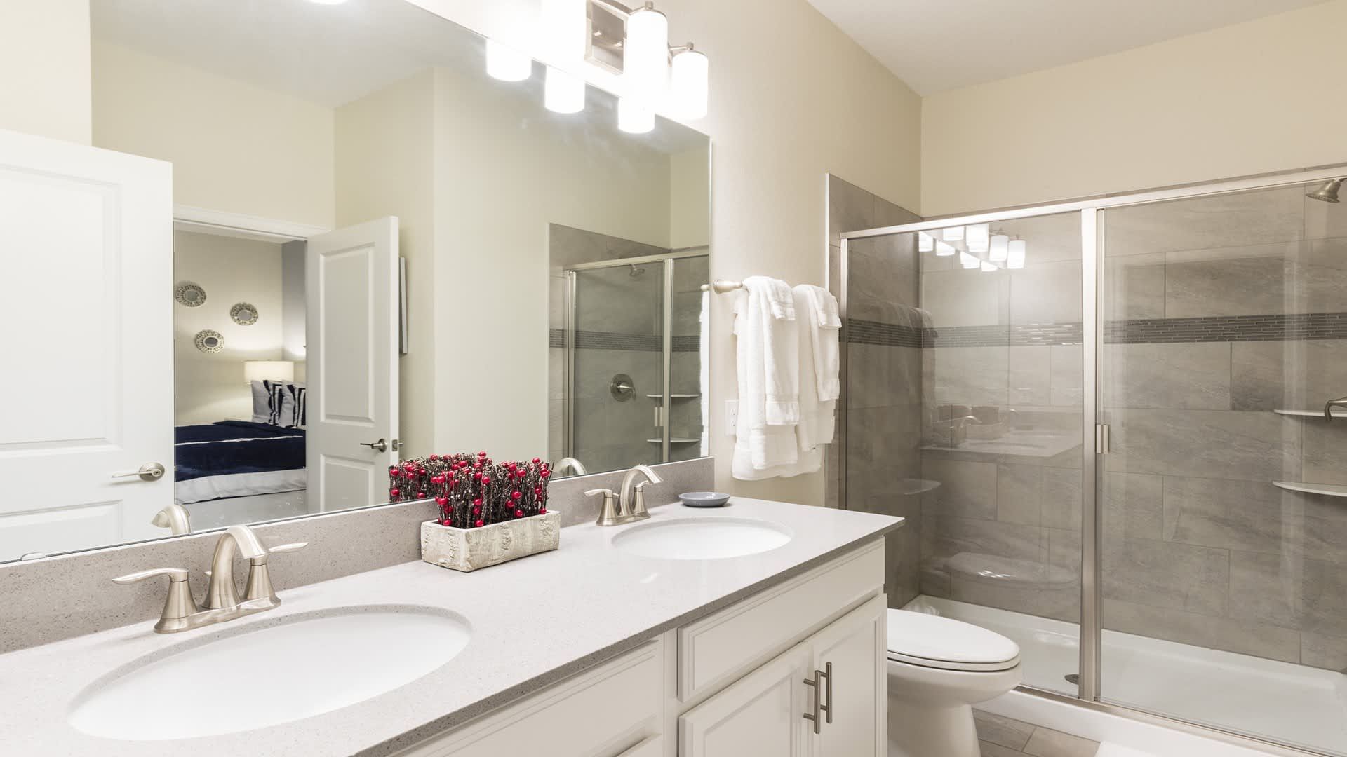 Elegant double vanity bath with glass shower, modern lighting, and sleek finishes.