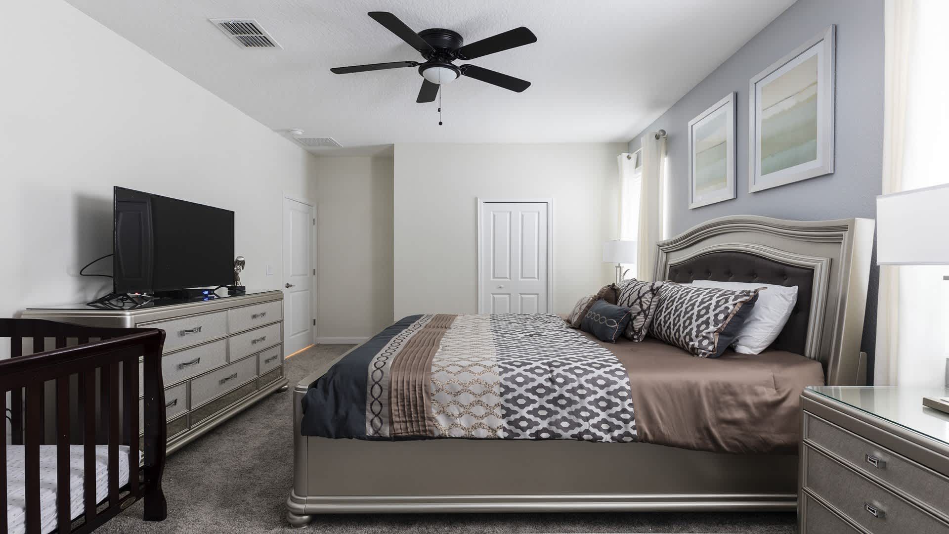 Spacious king bedroom with TV, elegant decor, and a convenient crib for families.