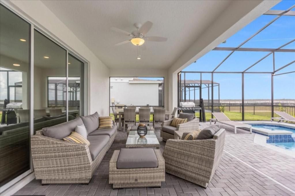 Spacious covered patio with comfy seating, ceiling fan, and screened-in pool views.