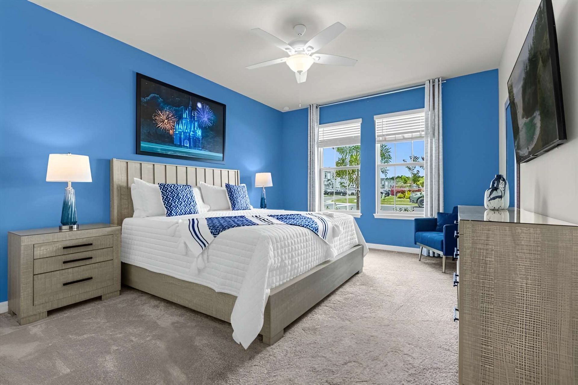 Bright ocean-themed bedroom with king bed, bold blue walls, and tropical window views.