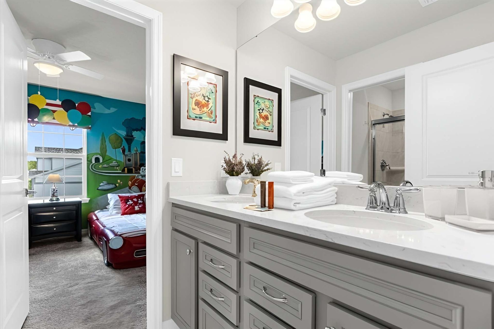 Bright double-sink bathroom with gray vanity and access to colorful themed bedroom.