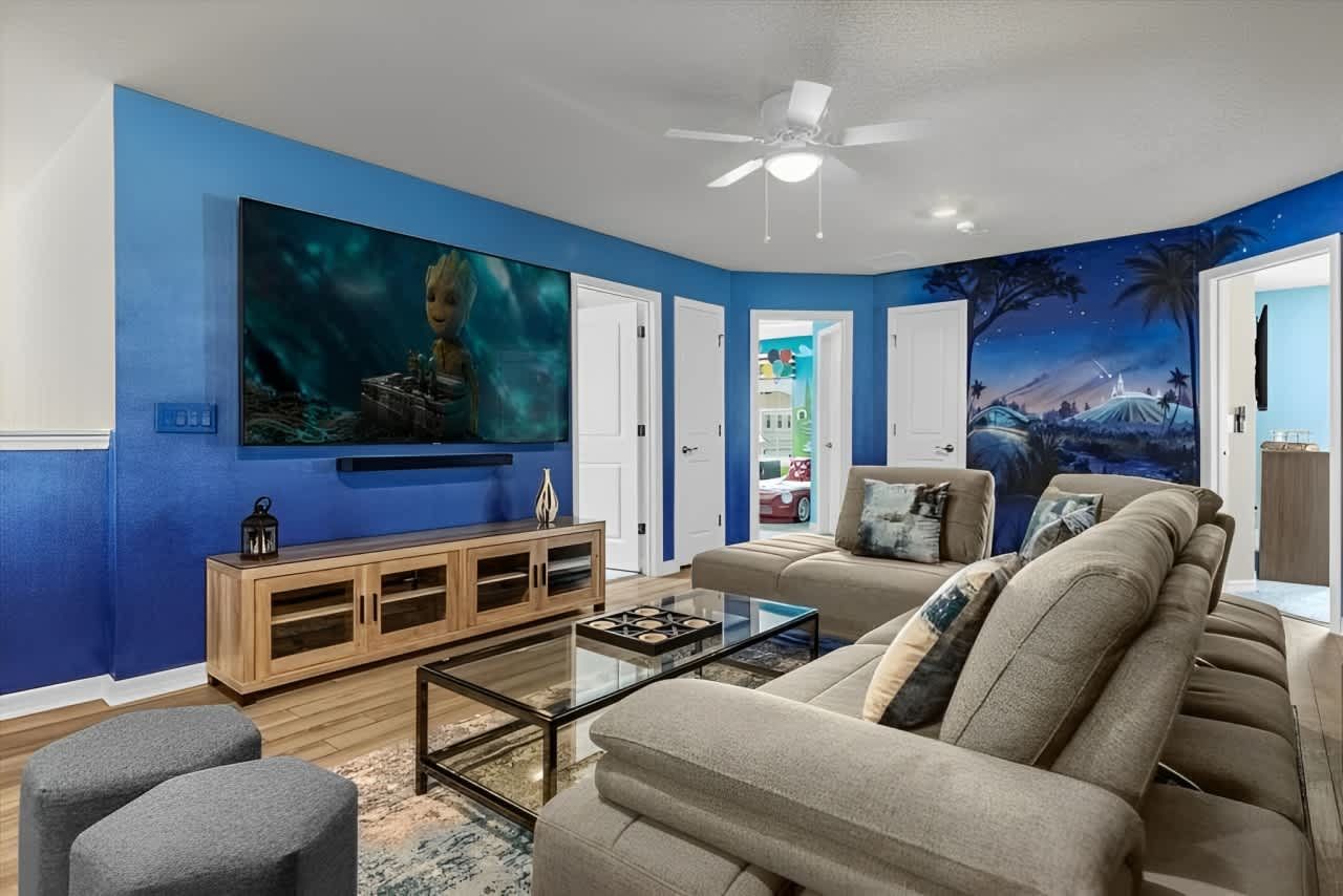 Cozy movie lounge with large sectional, themed mural, and giant TV for family fun.