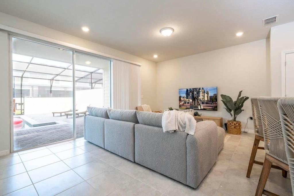 Open-concept living room with large TV, cozy seating, and poolside views.