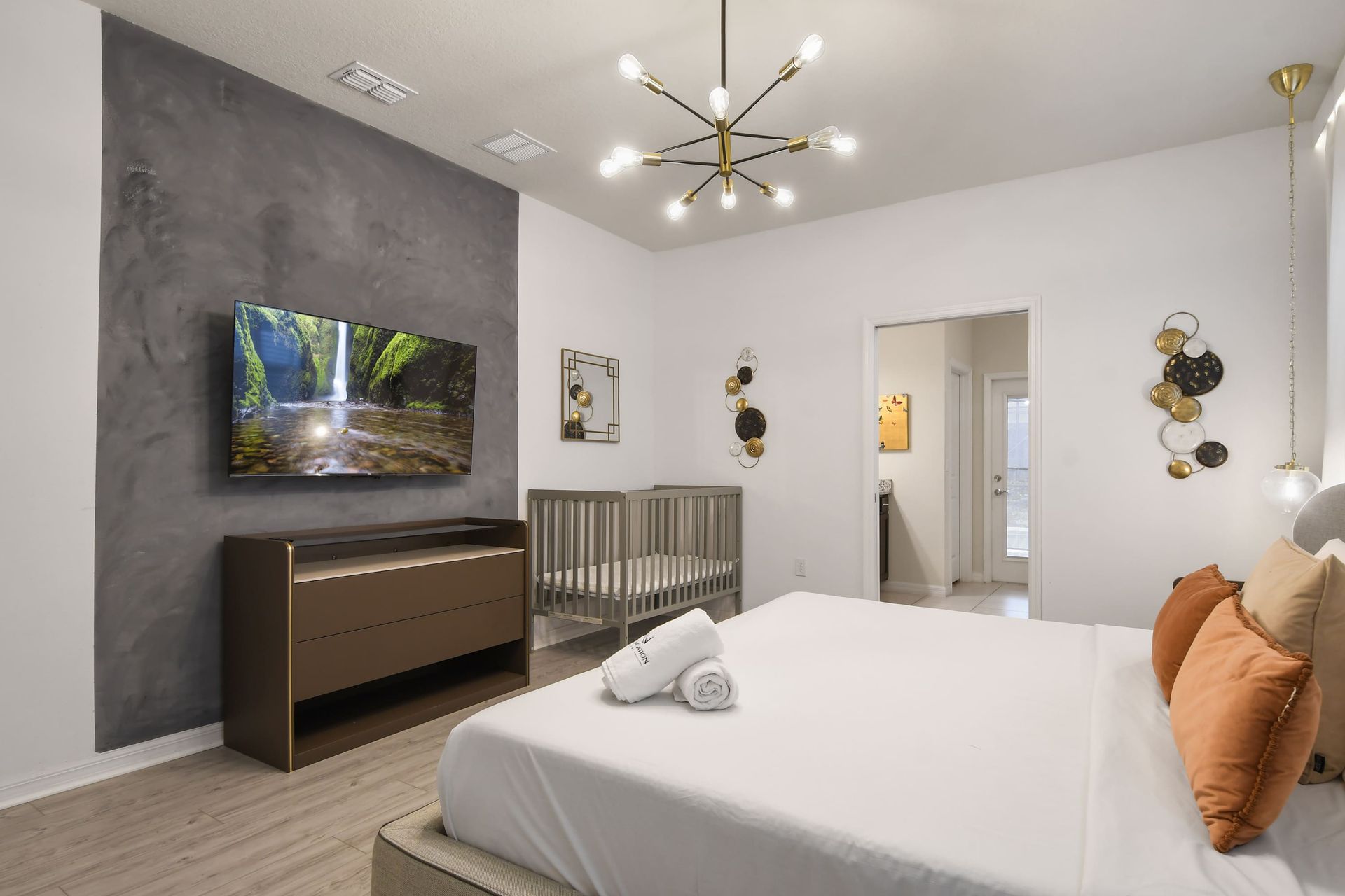 Chic bedroom with king bed, smart TV, modern crib, and warm ambient lighting.
