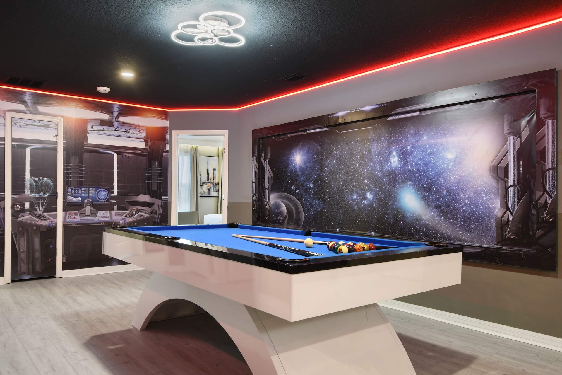 Futuristic game room with curved pool table, space murals, and vibrant LED glow.