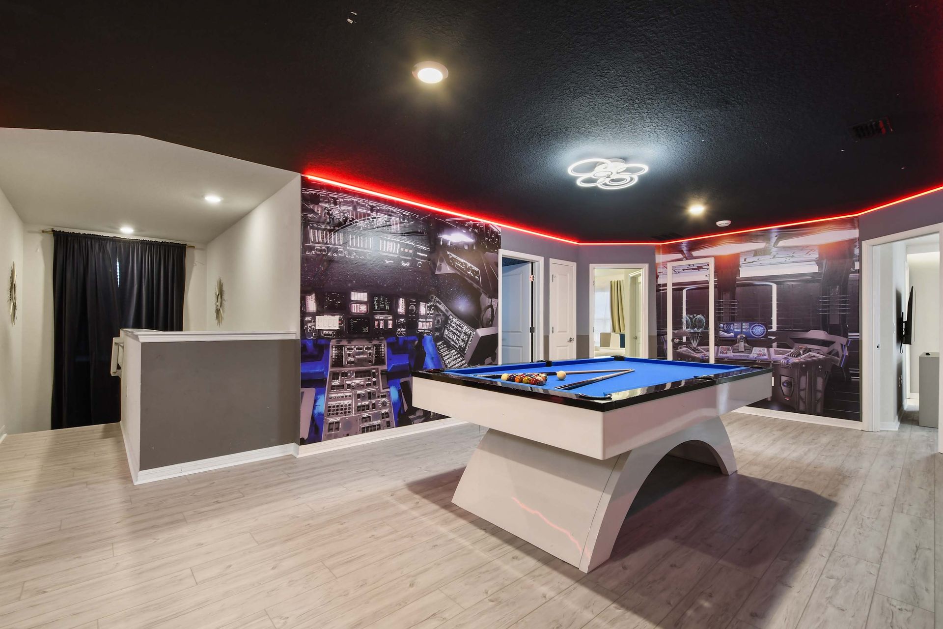 Stylish sci-fi game room with curved pool table, bold LED lighting, and space art.