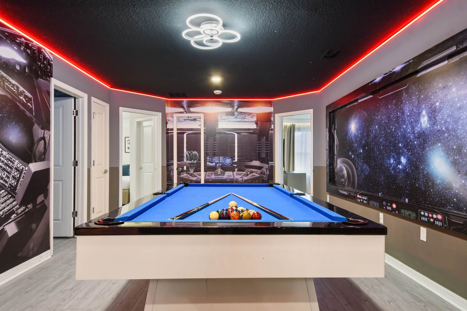 Futuristic game room with LED lighting, galaxy walls, and a sleek blue pool table.