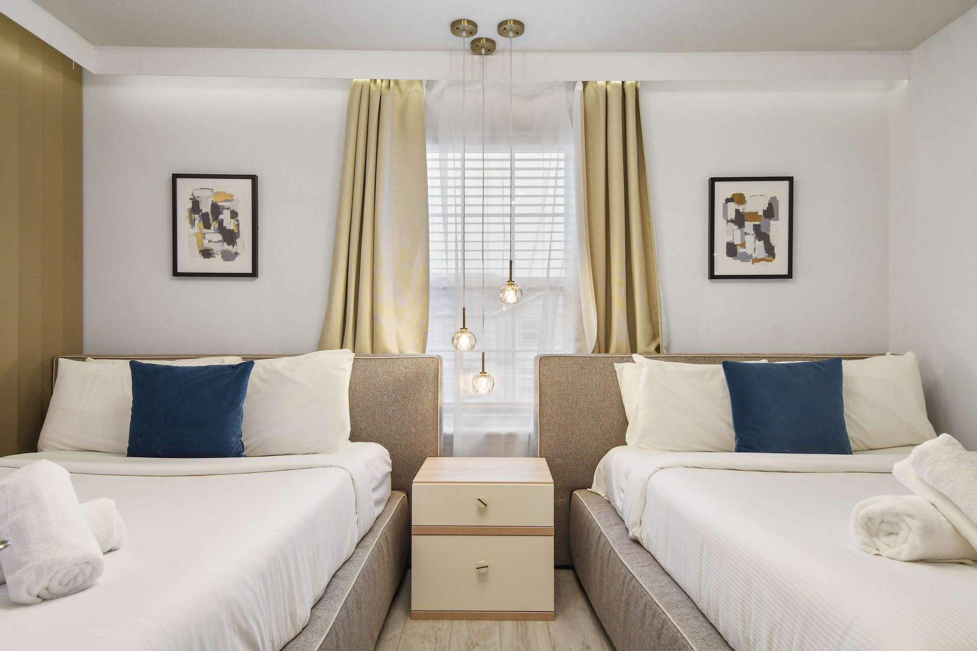 Bright and cozy room with two plush beds, modern decor, and elegant lighting.