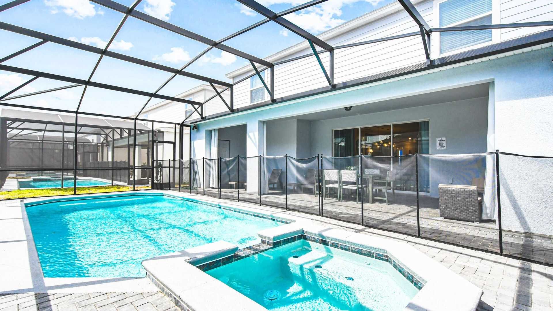 Bright screened-in pool and spa with safety fence, outdoor dining, and lounge space.