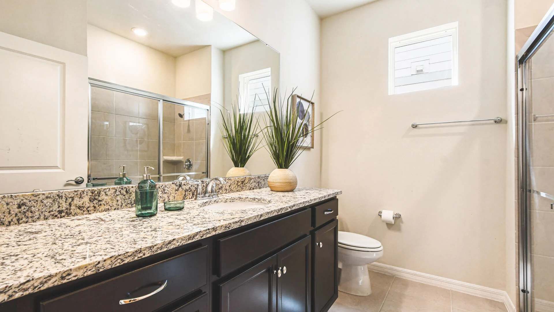 Modern bathroom with granite countertops, double sinks, and a glass-enclosed shower.