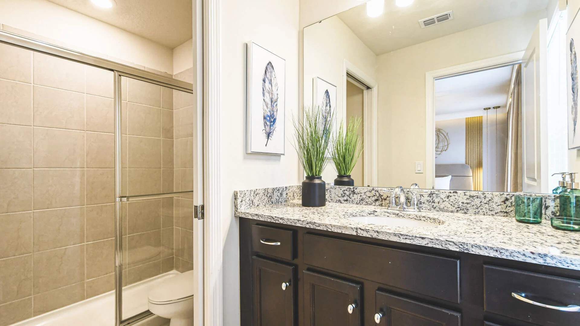Bright bathroom with granite countertop, sleek tile shower, and modern finishes.