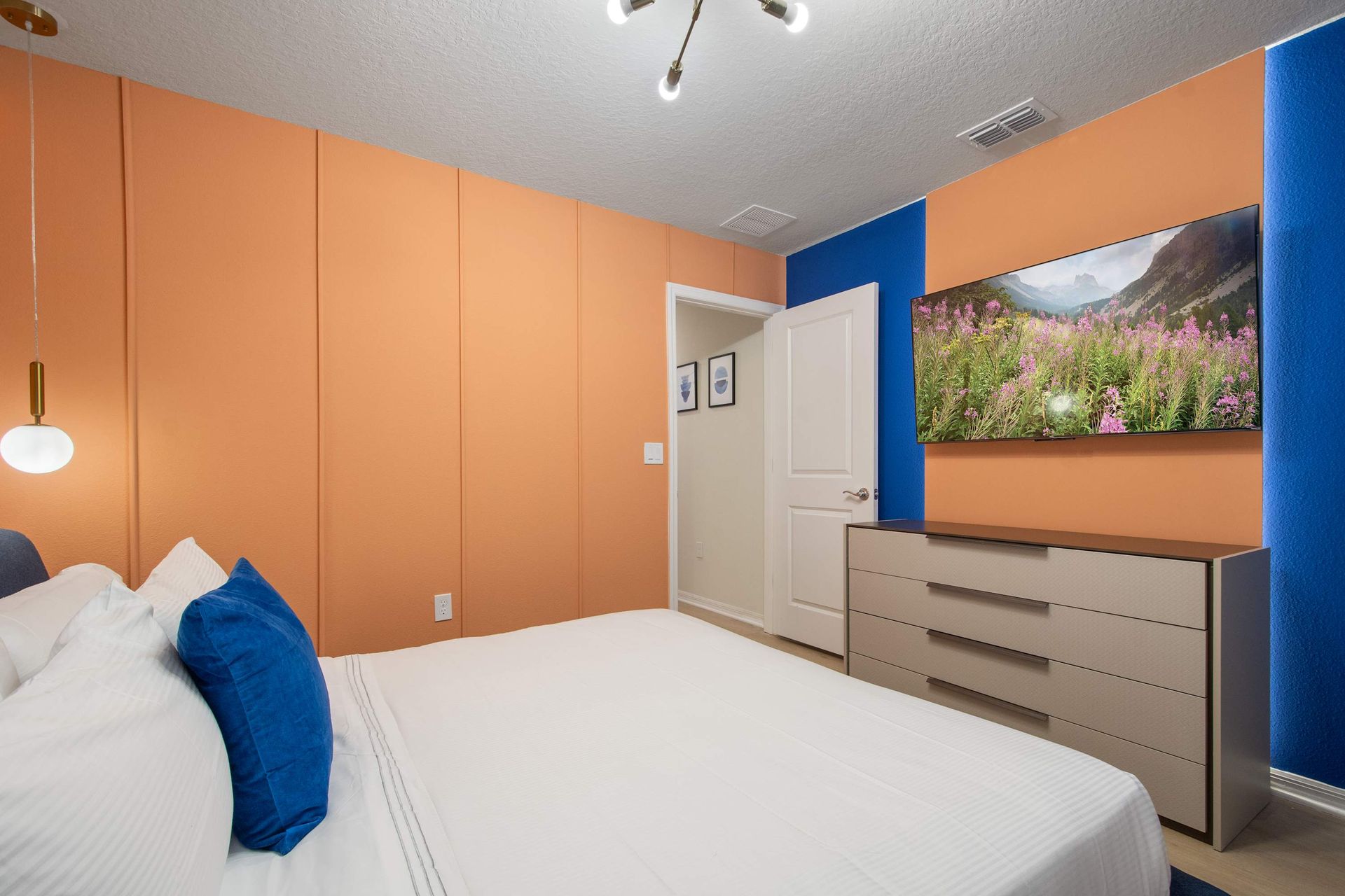 Vibrant bedroom with bold accent walls, cozy bed, and large smart TV.