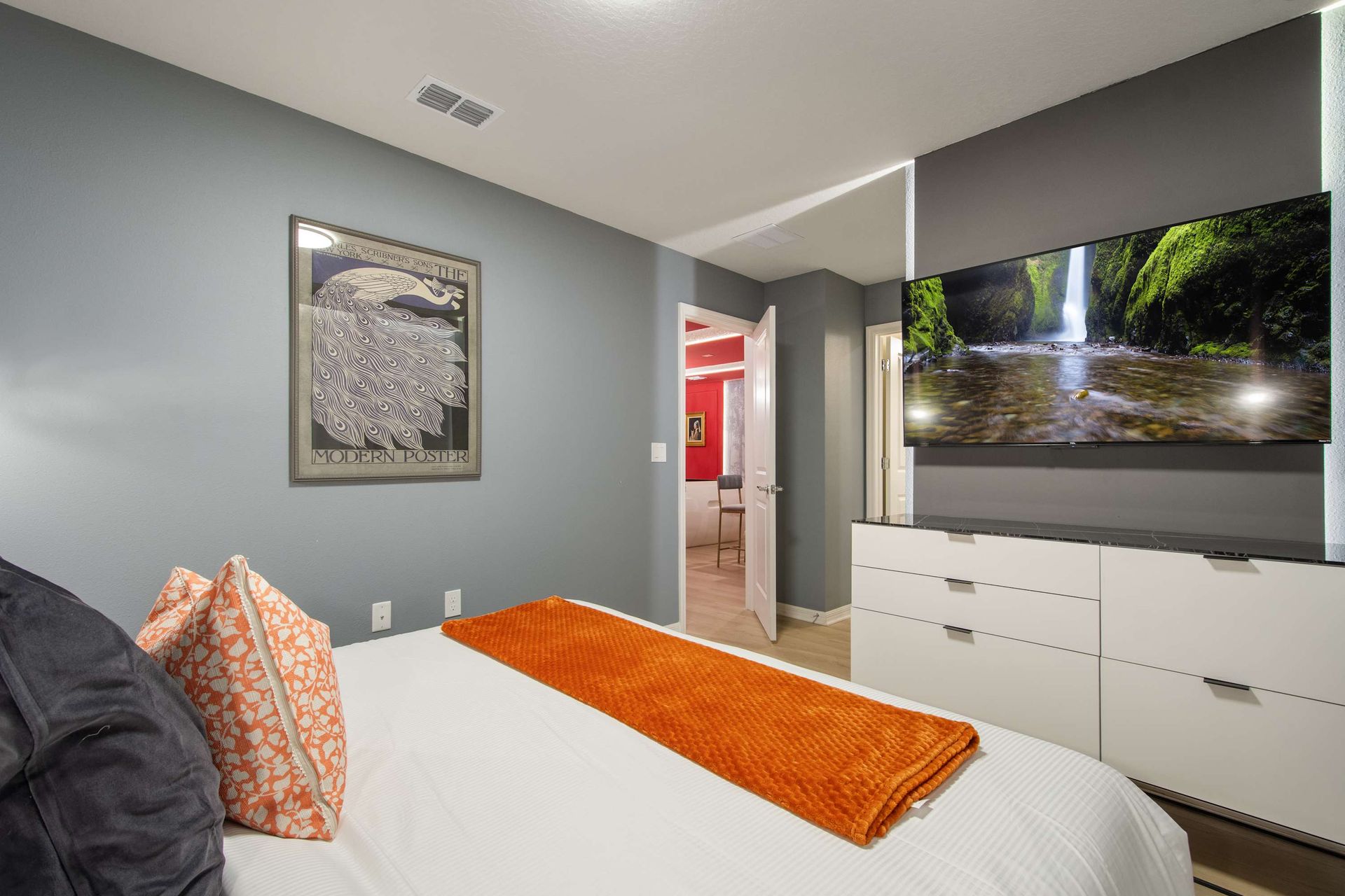 Cozy modern bedroom with sleek dresser, smart TV, and warm accent touches.