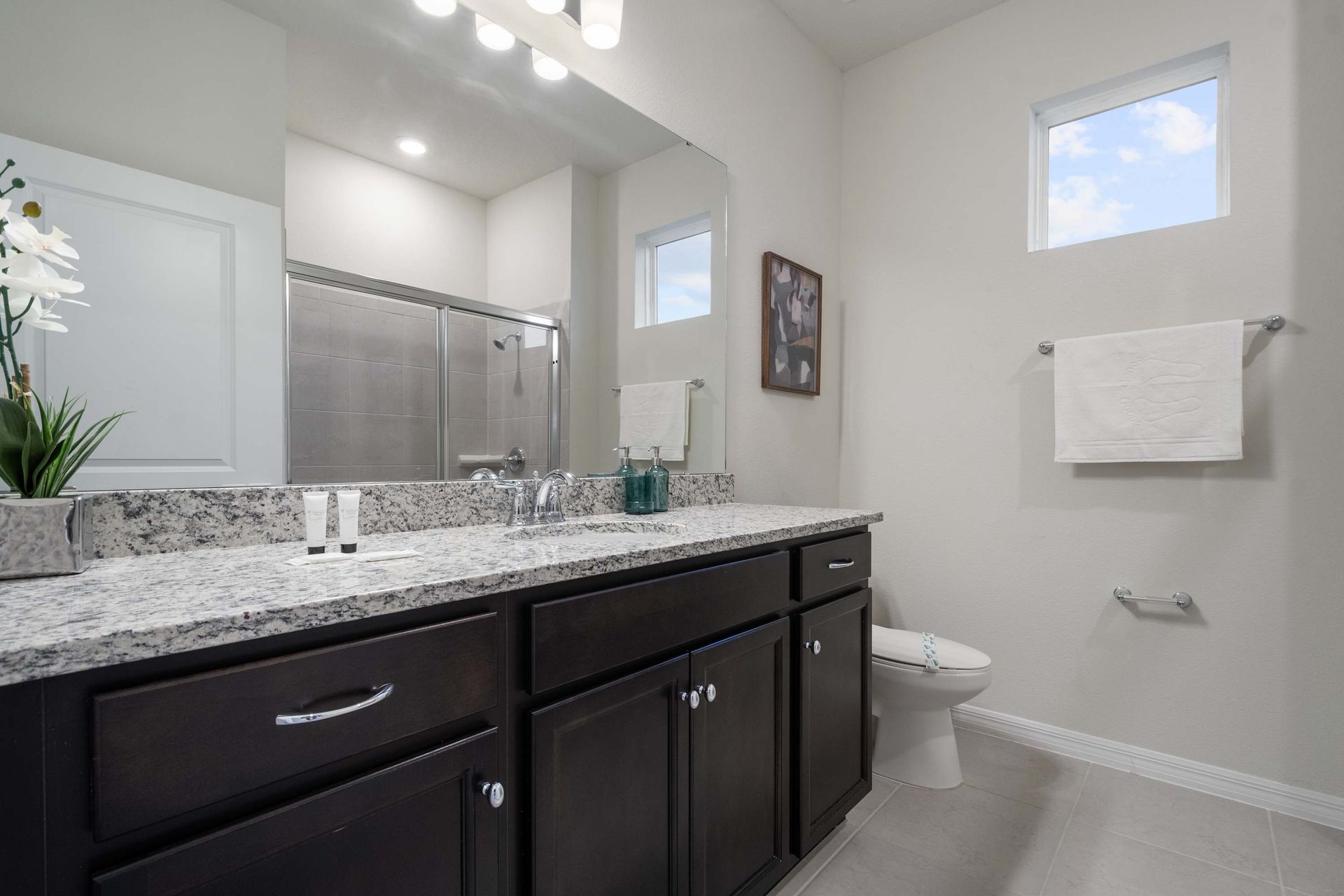 Spacious bathroom with double vanity, granite counters, and a sleek glass shower.