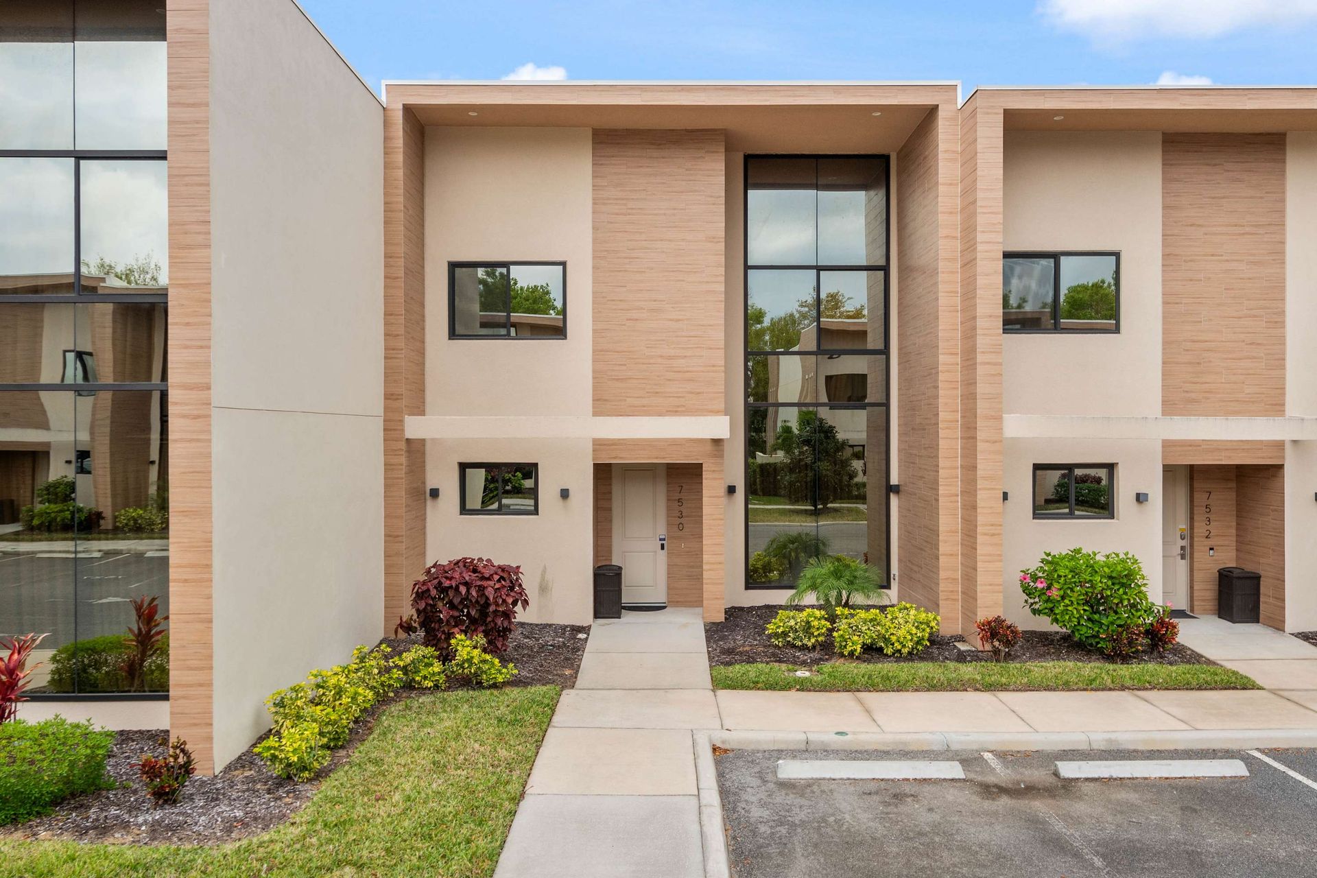 Modern townhouse with sleek design, large windows, lush landscaping, and parking
