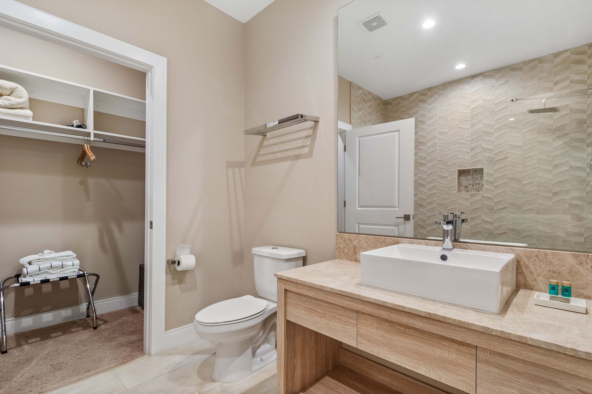 Spacious bathroom with walk-in closet, modern vanity, and stylish tiled shower wall
