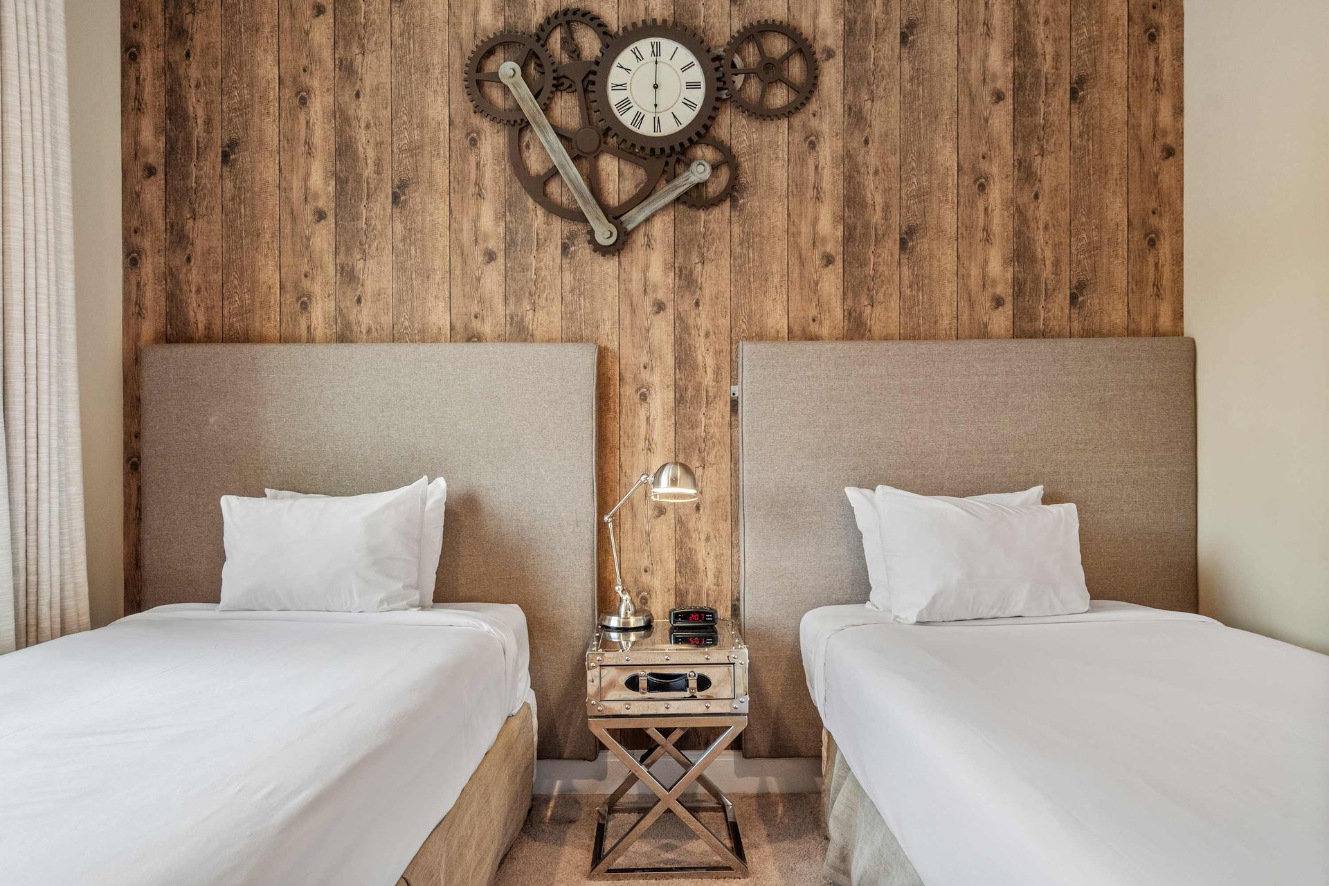 Cozy twin bedroom with industrial clock decor, rustic wood wall, and soft lighting
