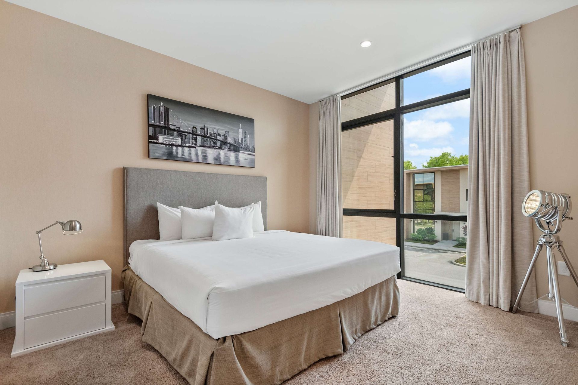 Modern bedroom with king bed, floor-to-ceiling window, and chic urban decor
