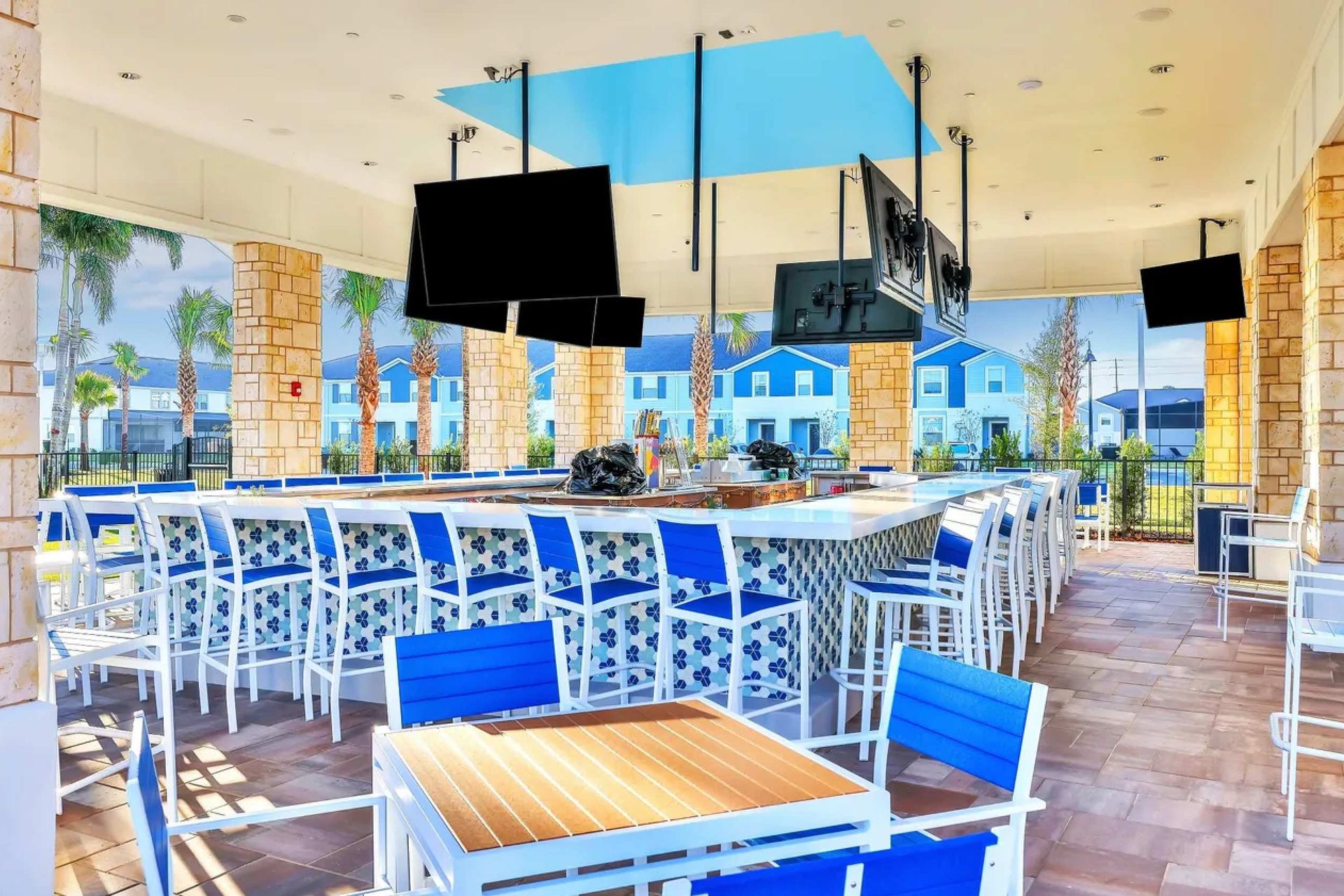 Open-air resort bar with multiple TVs, modern seating, and views of palm trees
