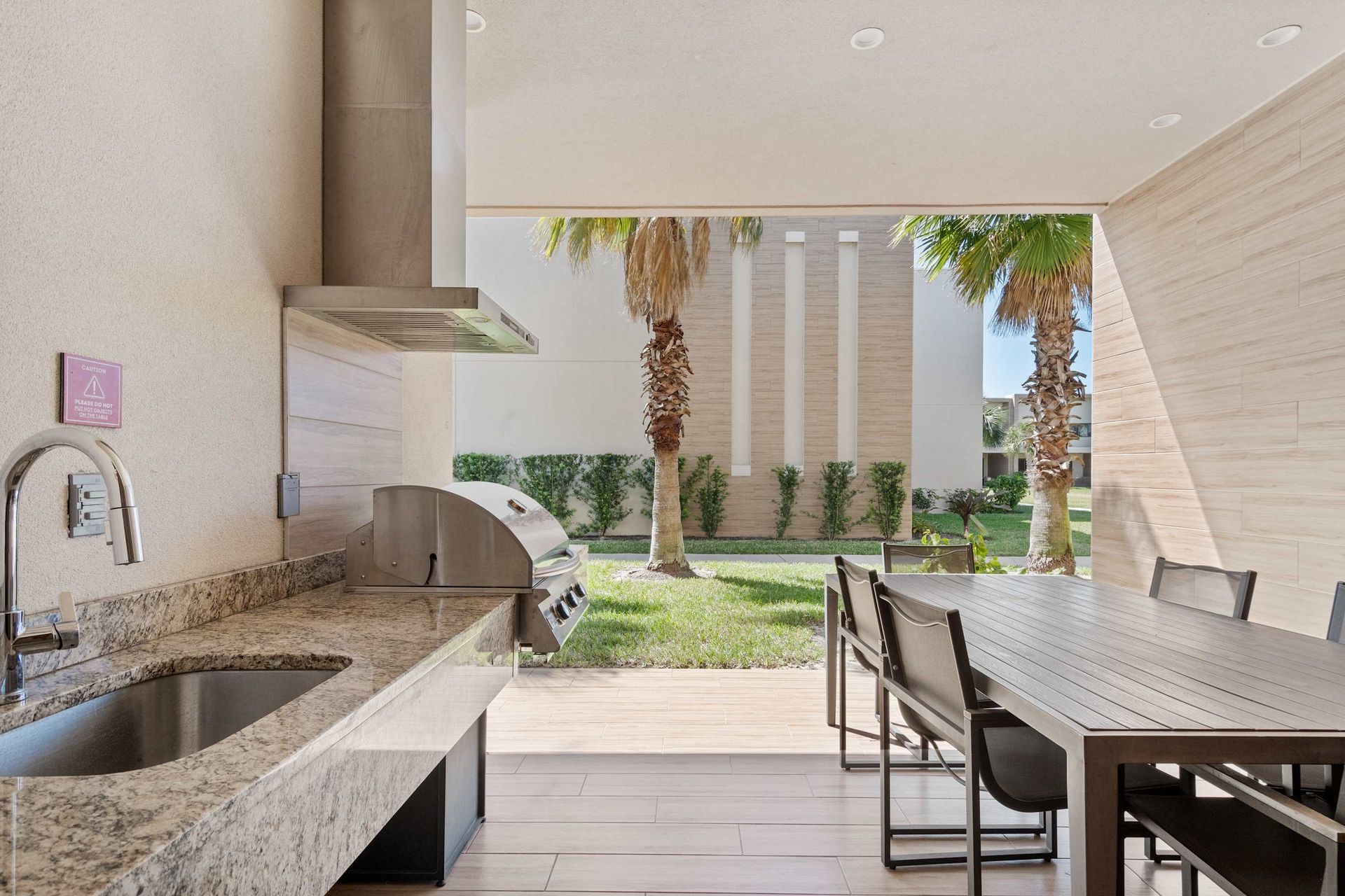 Outdoor kitchen with built-in grill, sink, dining area, and serene palm-lined views
