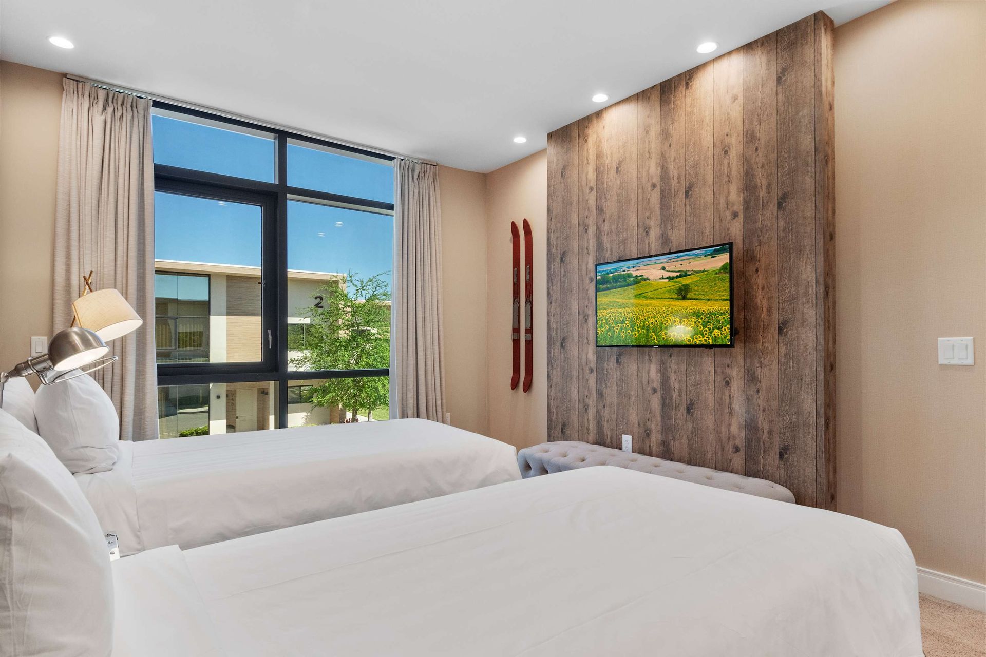 Cozy twin bedroom with rustic charm, large windows, and a mounted smart TV
