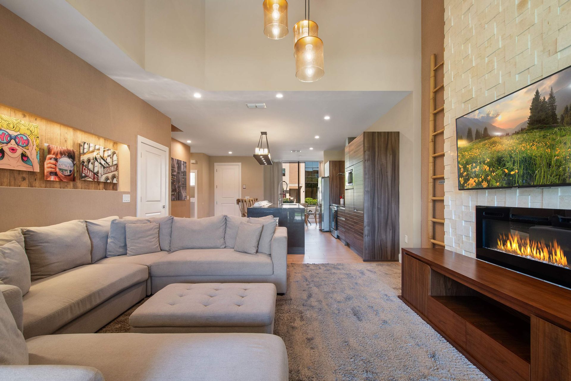 Cozy living room with fireplace, plush sectional, modern art, and open kitchen.
