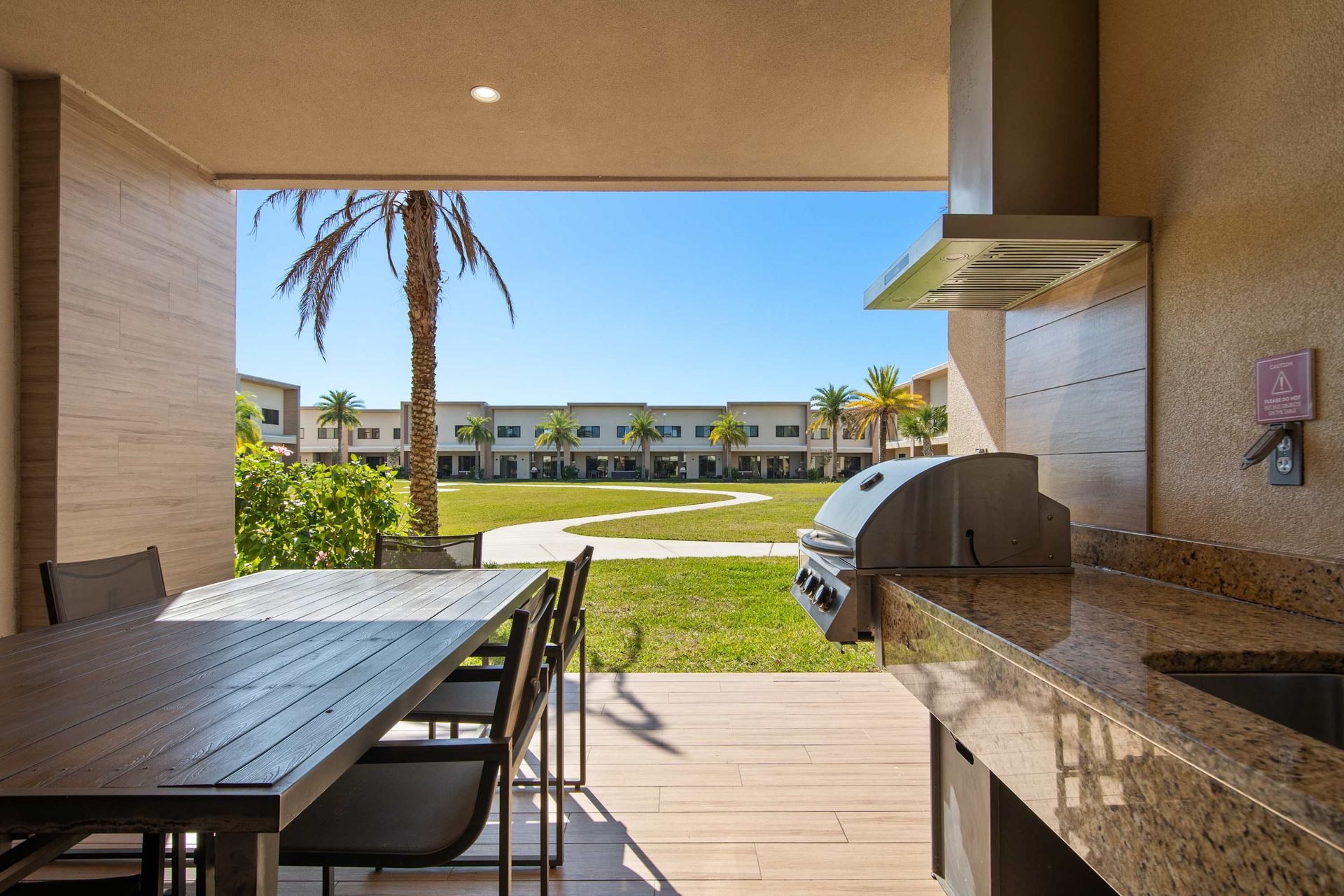 Covered patio with dining table, built-in grill, and views of lush green courtyard.
