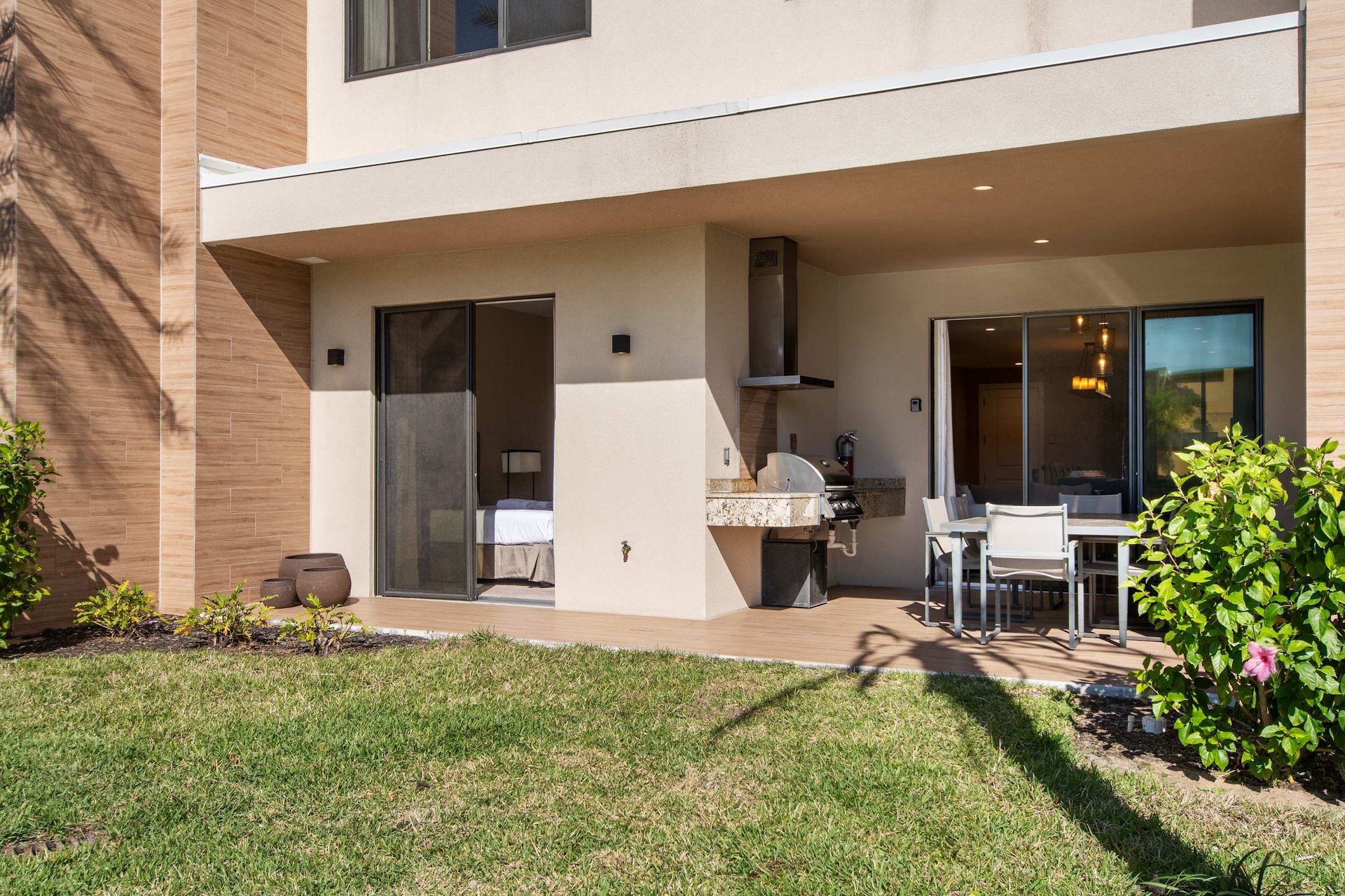 Covered patio with grill, dining area, and sliding doors opening to a green backyard.
