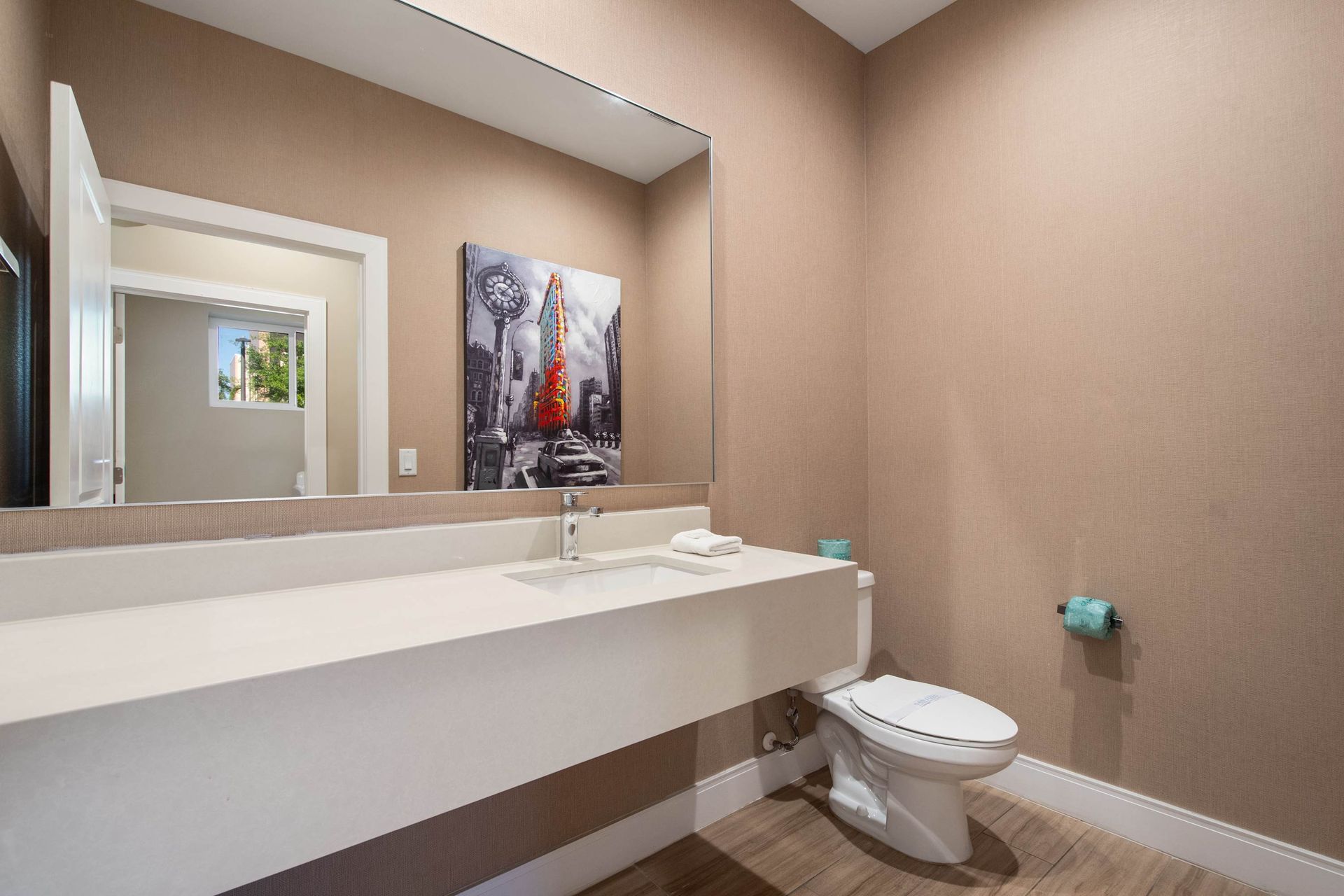 Contemporary half bath with sleek vanity, large mirror, modern art, and warm tones.
