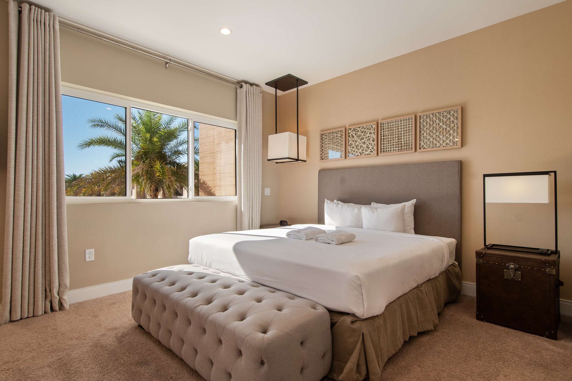 Serene bedroom with king bed, plush bench, large window, and warm elegant decor.
