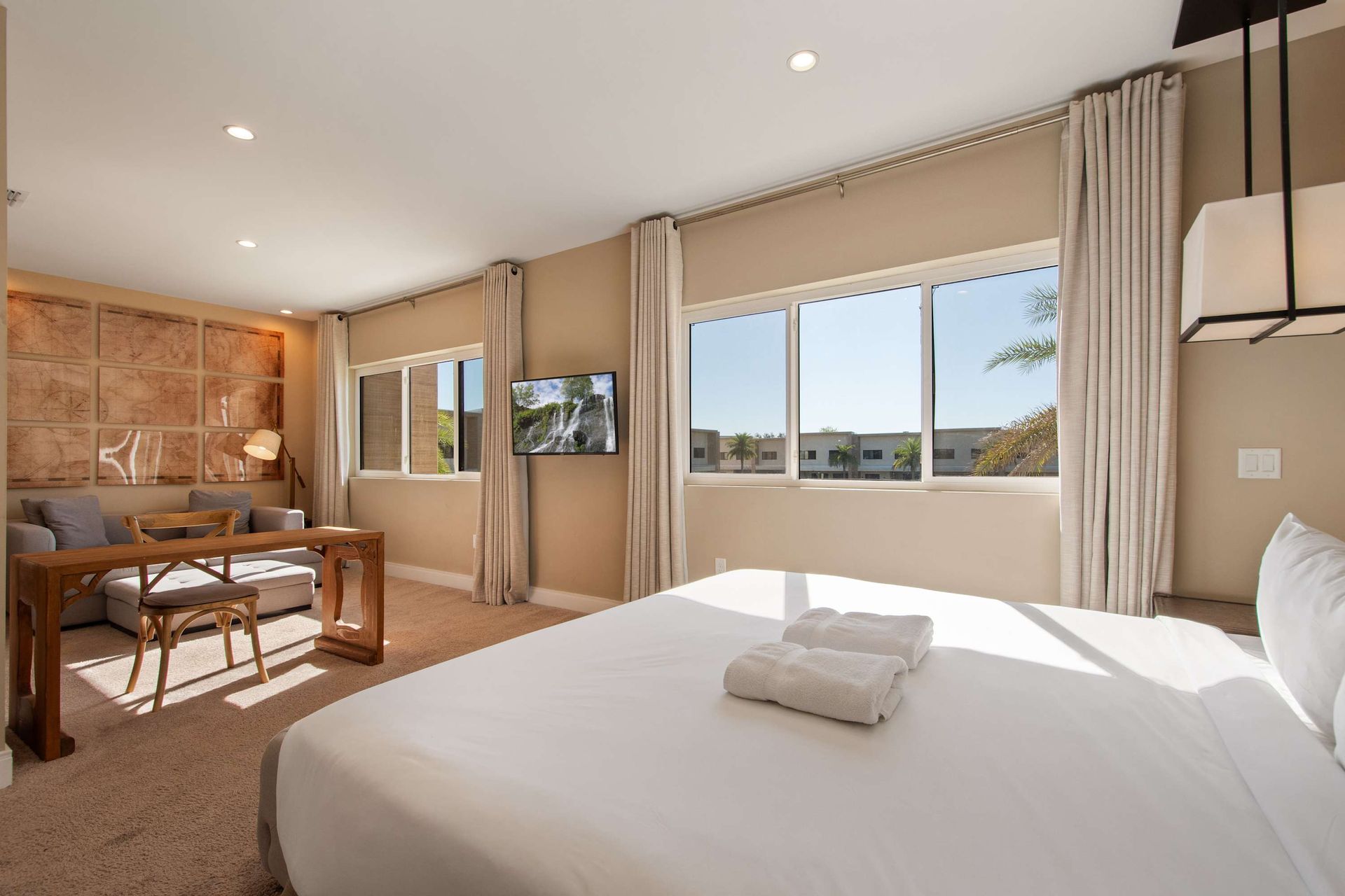 Sunny bedroom with king bed, workspace, comfy seating, and big windows with a view.
