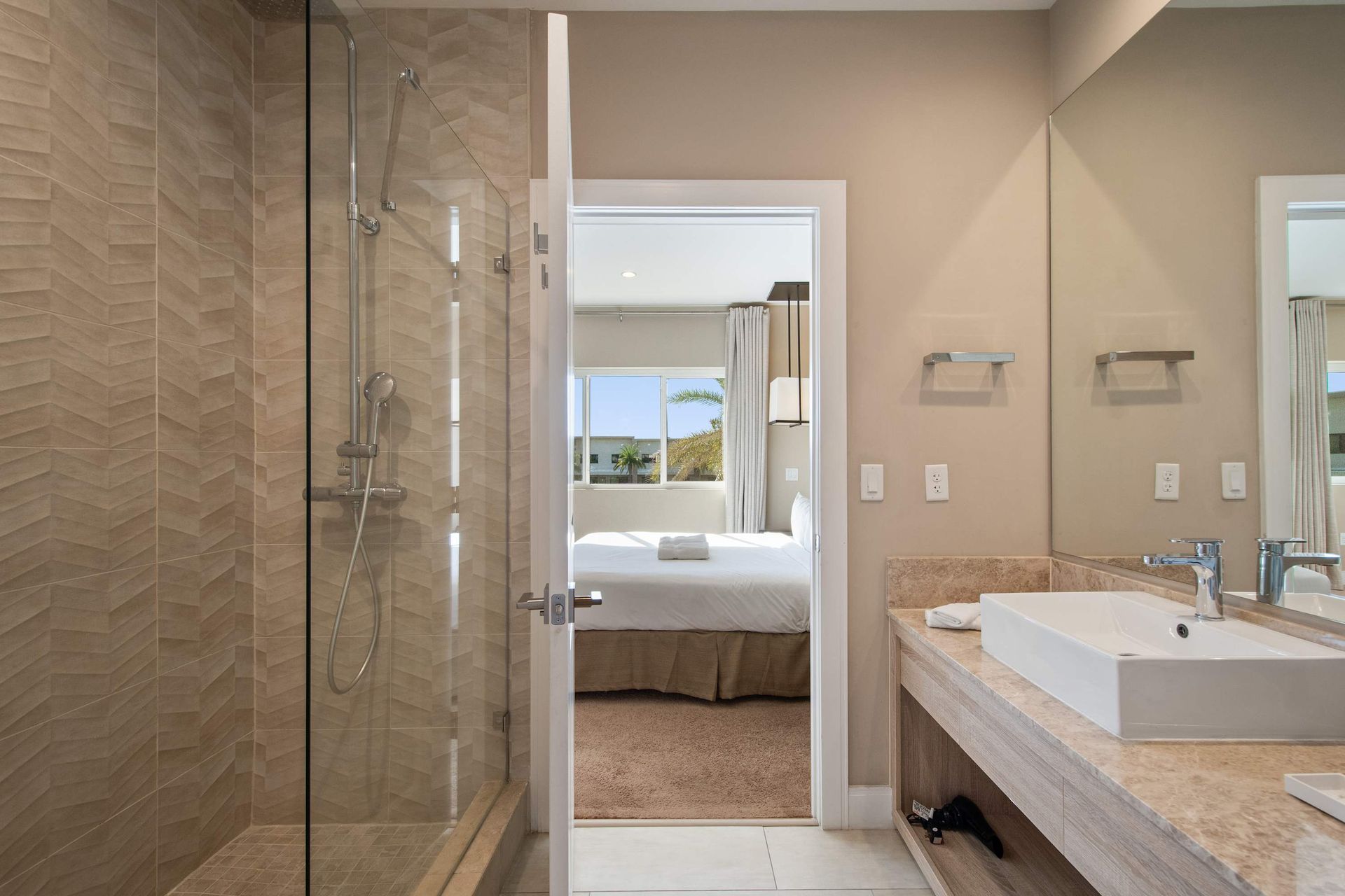 Modern ensuite bathroom with glass shower, large mirror, sleek vanity, and bright view.
