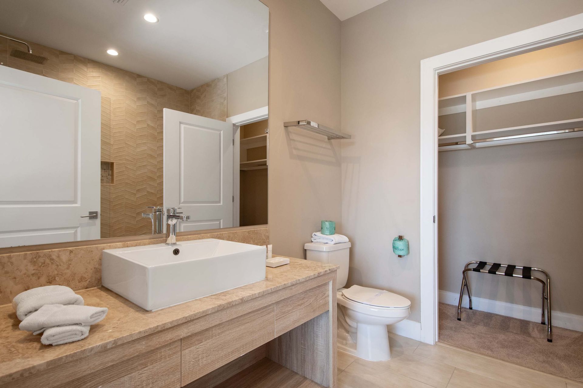 Modern bathroom with spacious vanity, walk-in closet, large mirror, and warm decor.
