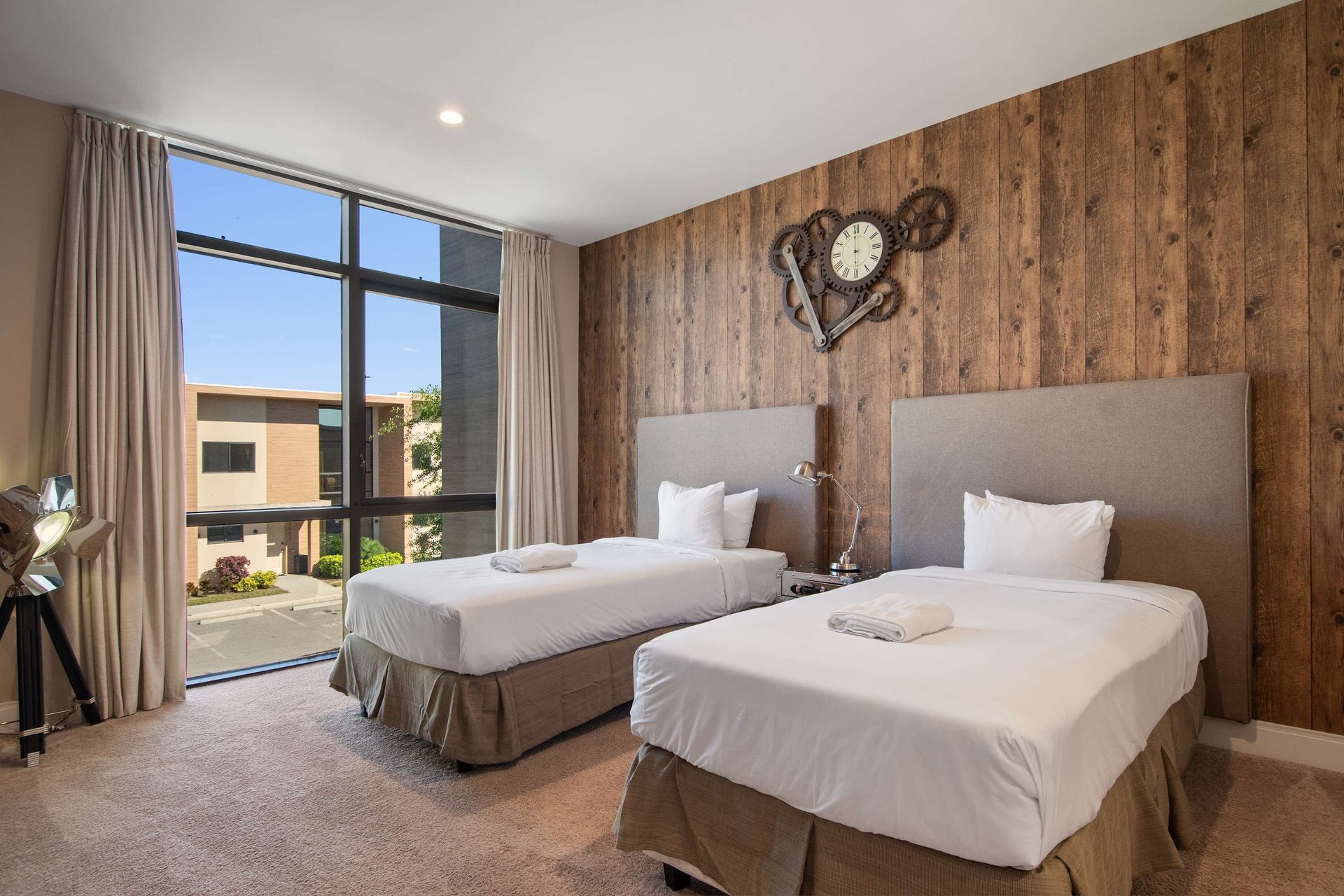 Rustic modern twin bedroom with large window, wood accent wall, and cozy decor.
