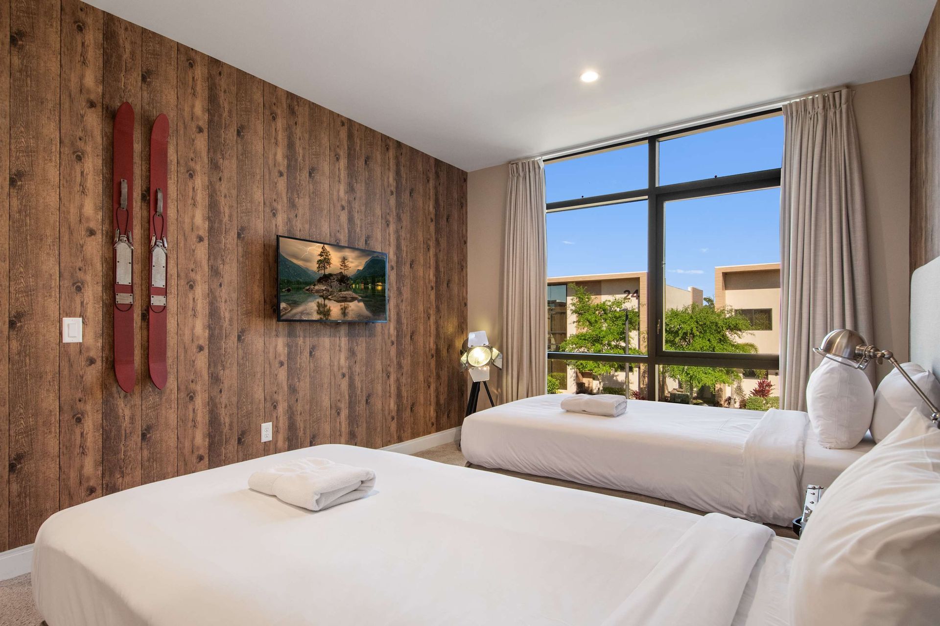 Cozy twin room with rustic wood wall, large window, modern decor, and garden view.
