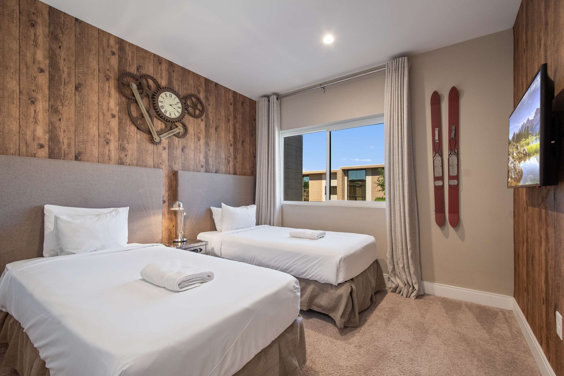 Rustic modern twin bedroom with large window, wood accent wall, and cozy decor.
