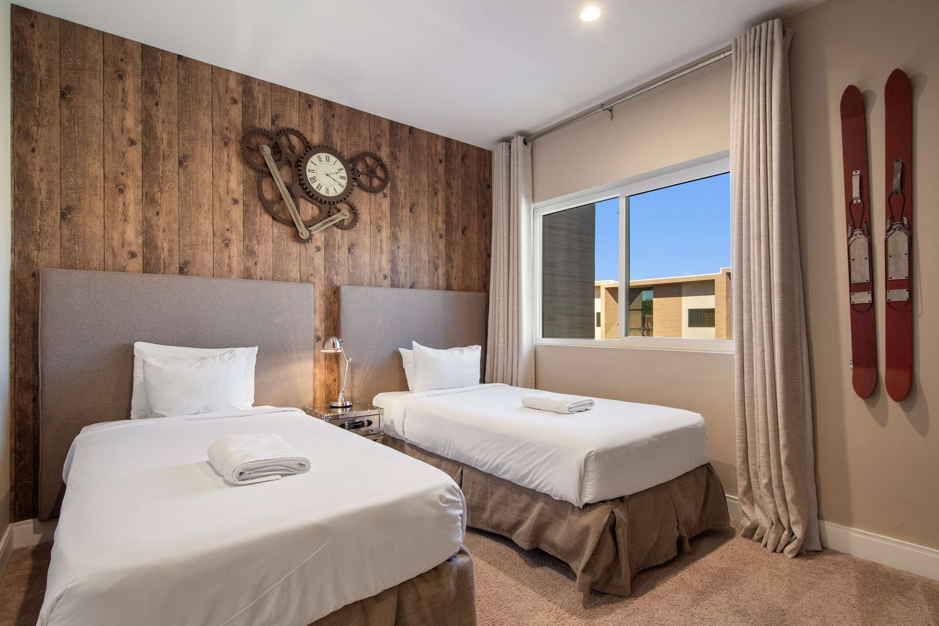 Cozy twin bedroom with rustic wood wall, unique clock decor, and warm inviting vibe.
